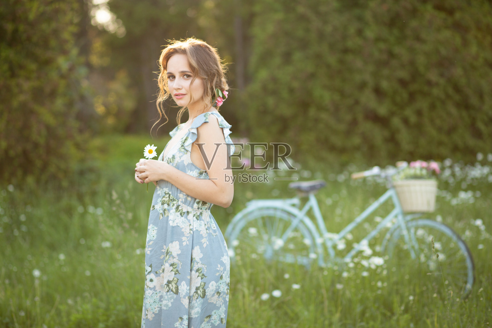 画像上一个美丽的女孩在森林里,抱着自行车,提着花篮,在阳光的照射下,穿着蓝色的花裙,夏日漫步照片摄影图片