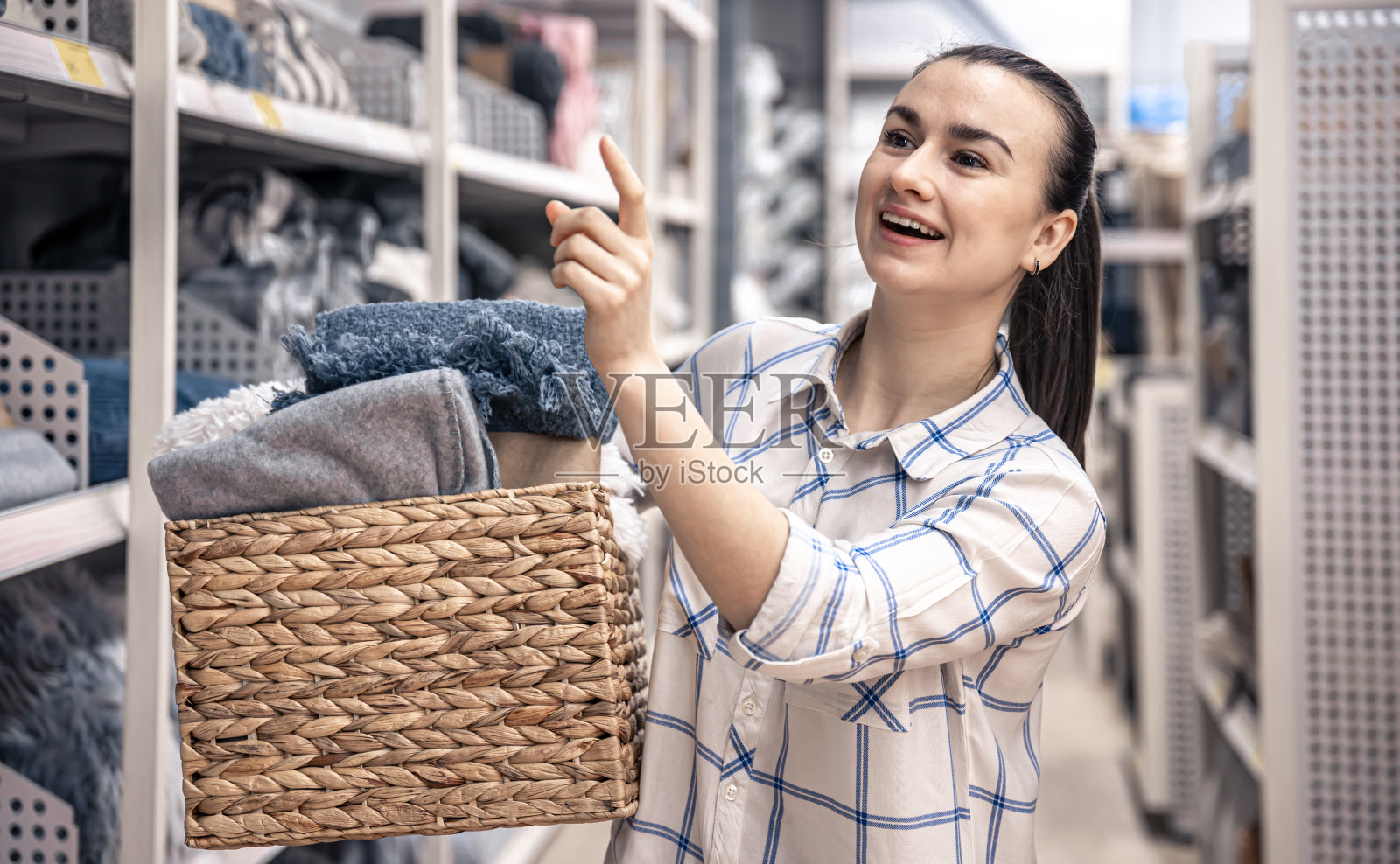 一个年轻的女人带着一个装满毯子的柳条篮子在一家家居装饰商店里。照片摄影图片