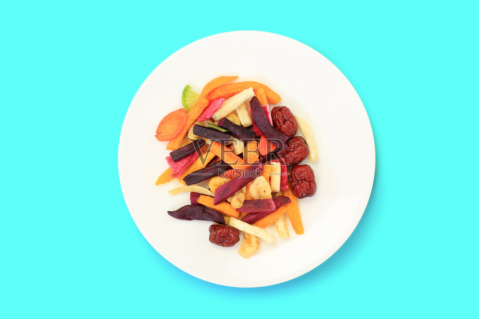 冷冻干燥的彩色酥脆水果和蔬菜在白色盘子上隔离在青色背景。混合干粮保健。俯视图照片摄影图片