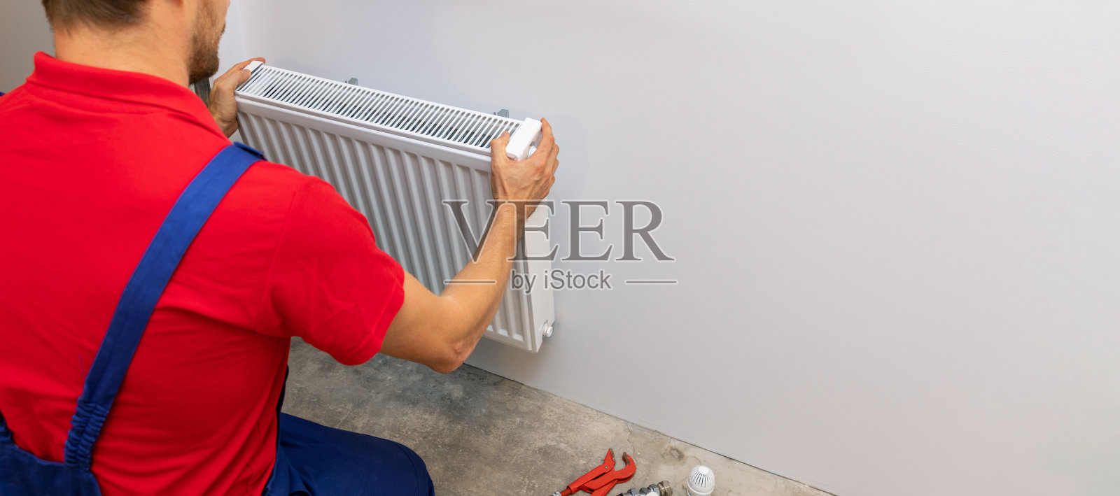 有人在墙上安装白色金属散热器。住宅供暖系统。本空间照片摄影图片