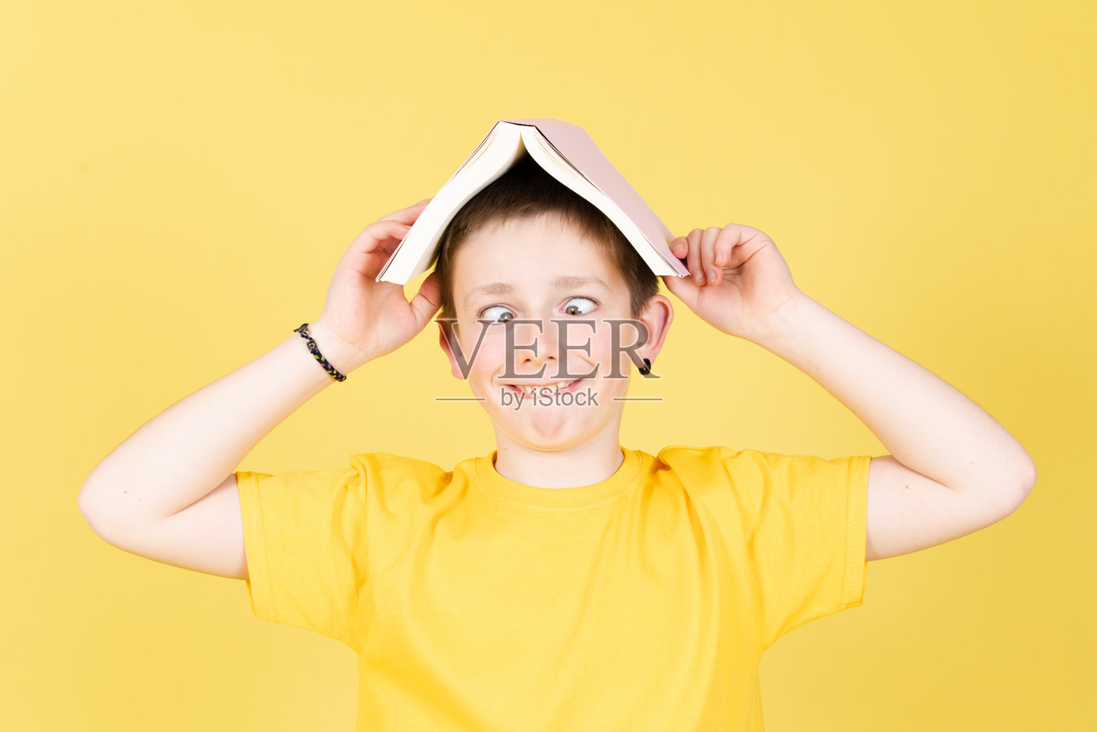 男孩做鬼脸,手里拿着一本书照片摄影图片