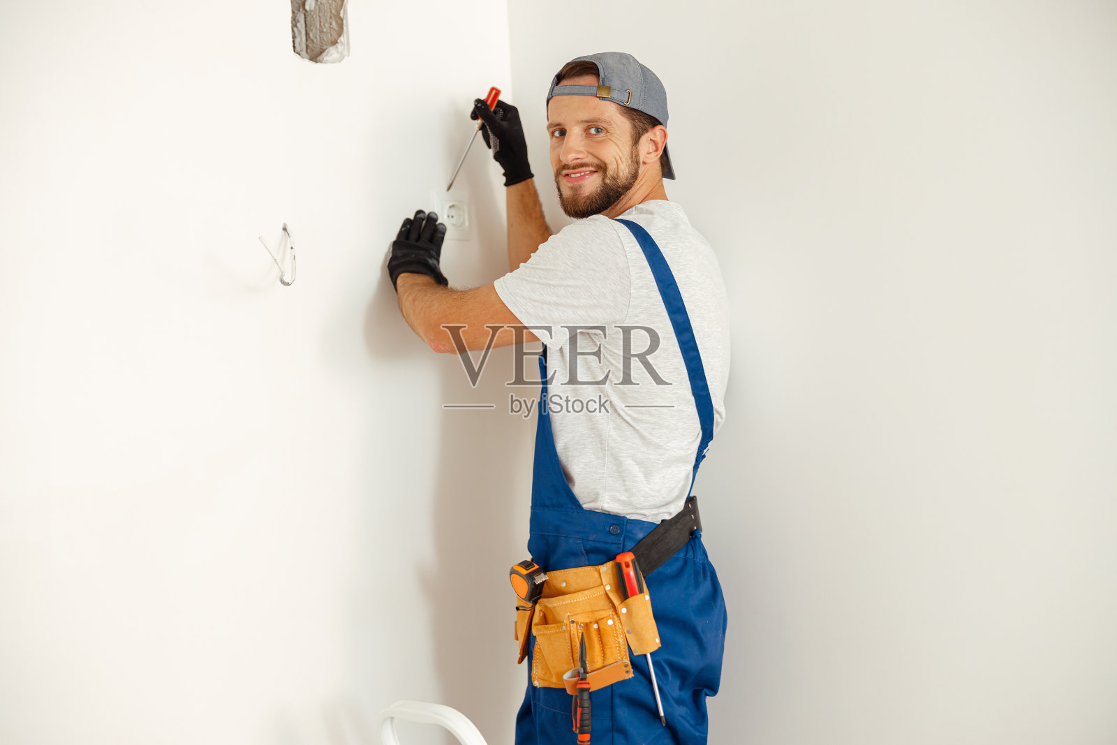 热情的电工,站在梯子上,微笑着看着摄像机照片摄影图片