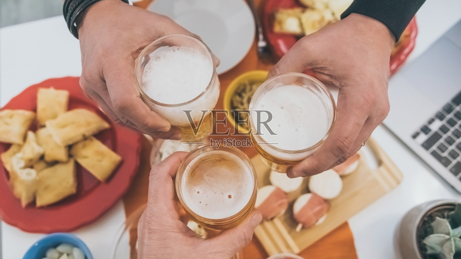 与朋友举杯共进晚餐。和一群朋友一起喝夏天的开胃酒。坐在桌子上,手里拿着许多食物和啤酒,让人心情愉快照片摄影图片