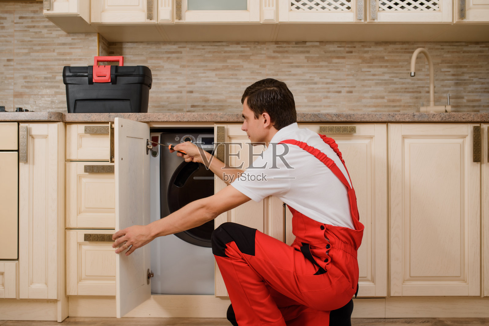 身着红色整体装修的工匠在厨房组装家具。照片摄影图片