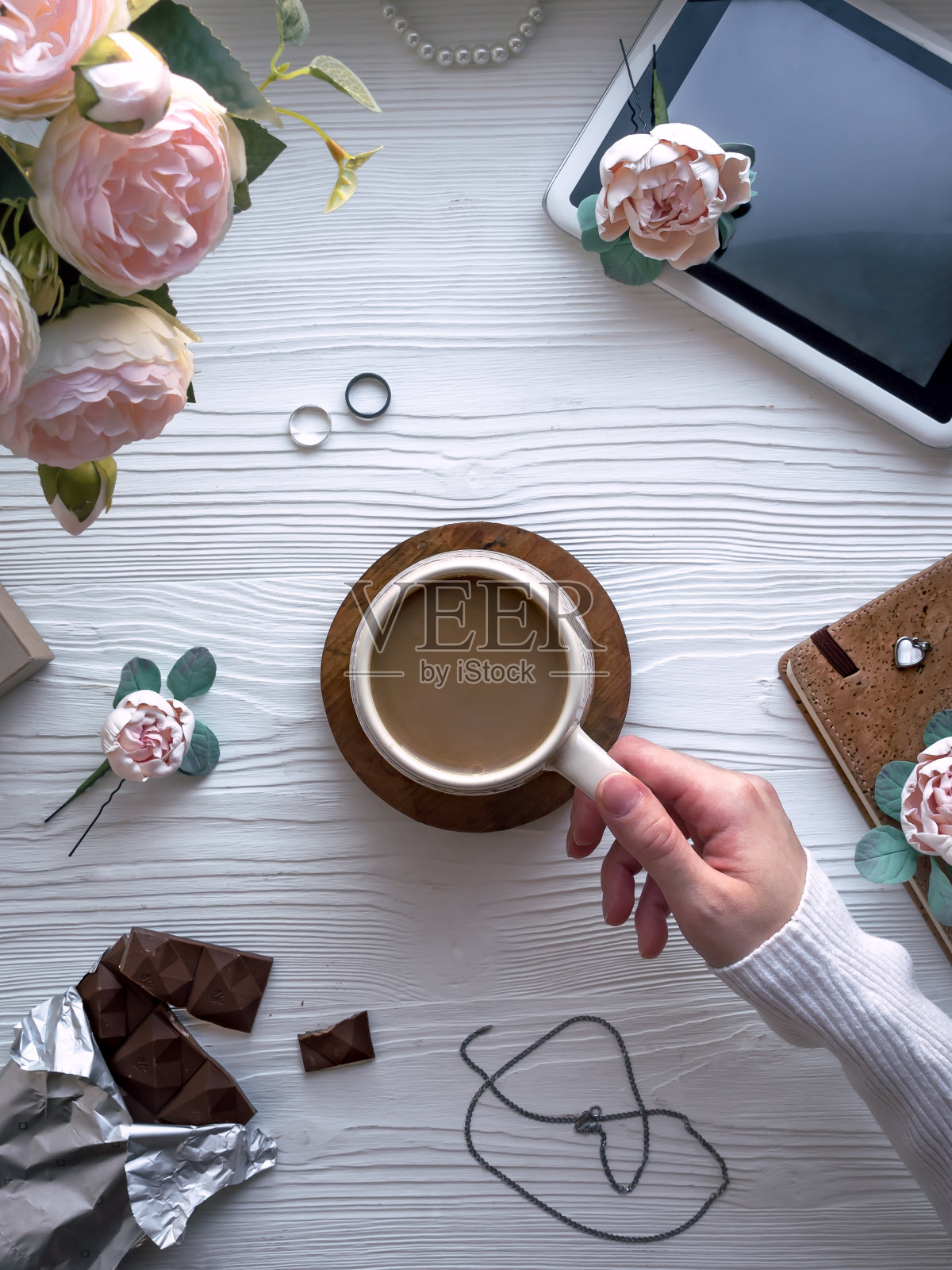 咖啡和牛奶在一个杯子里。喝咖啡:喝咖啡的过程记事本,写字板,笔,花,白色木桌上的装饰品。女性的桌面。咖啡休息。白色背景。从上面的观点照片摄影图片