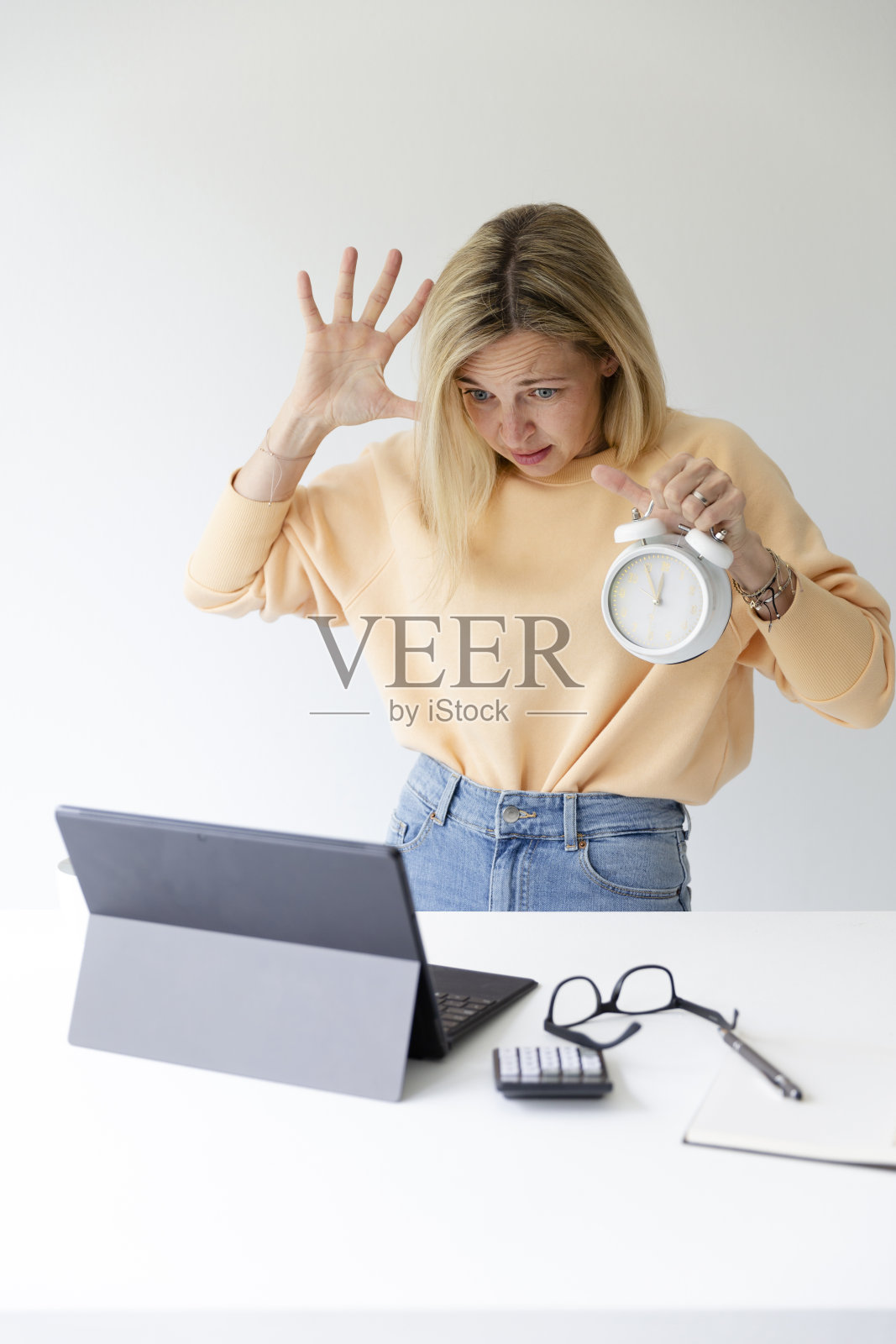 漂亮的金发女人站在吧台旁边手里拿着白色闹钟,时间是5点到12点照片摄影图片