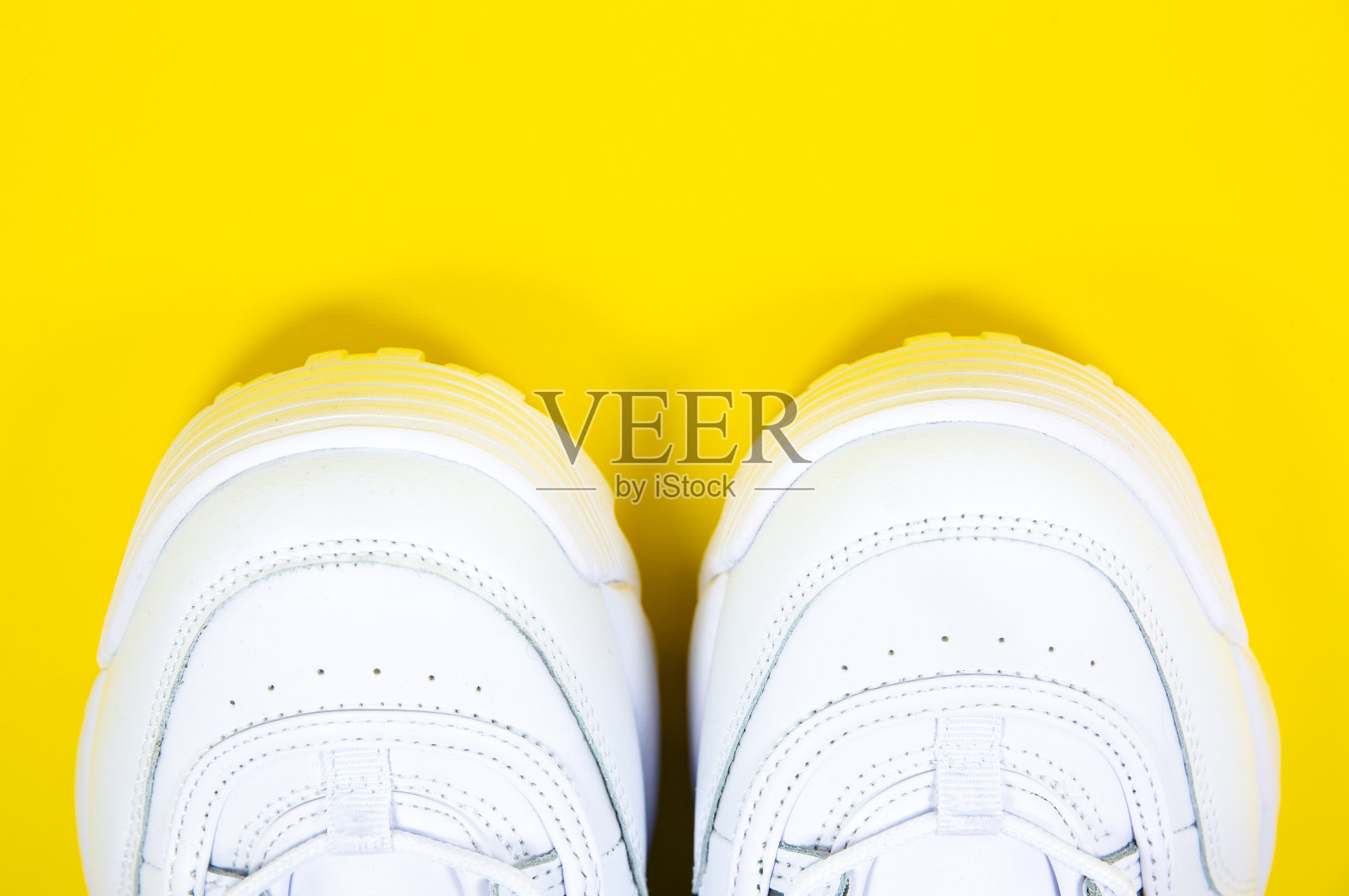 黄色背景上的现代运动鞋。白色真皮运动鞋,鞋底大,带尖钉。关闭了。照片摄影图片