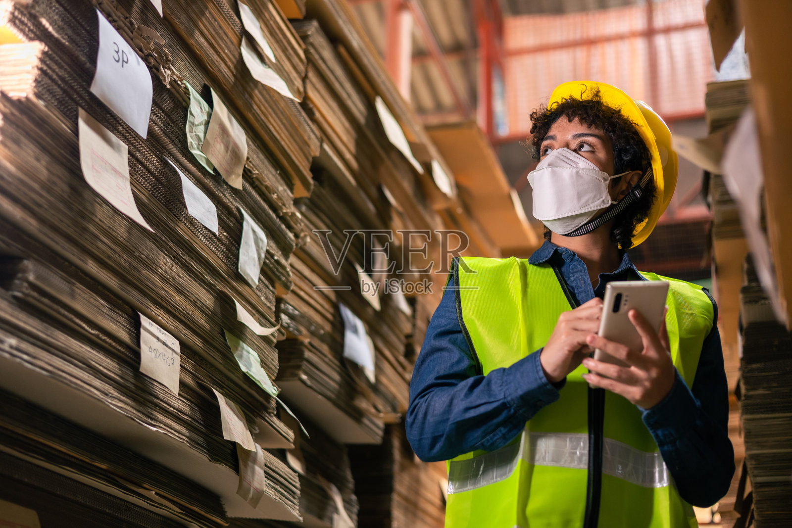工程师亚洲和非洲妇女戴安全帽和背心拿着剪贴板和笔记在纸上的汽车零部件仓库。产品及瓦楞纸板。本厂为纸张制造加工。照片摄影图片