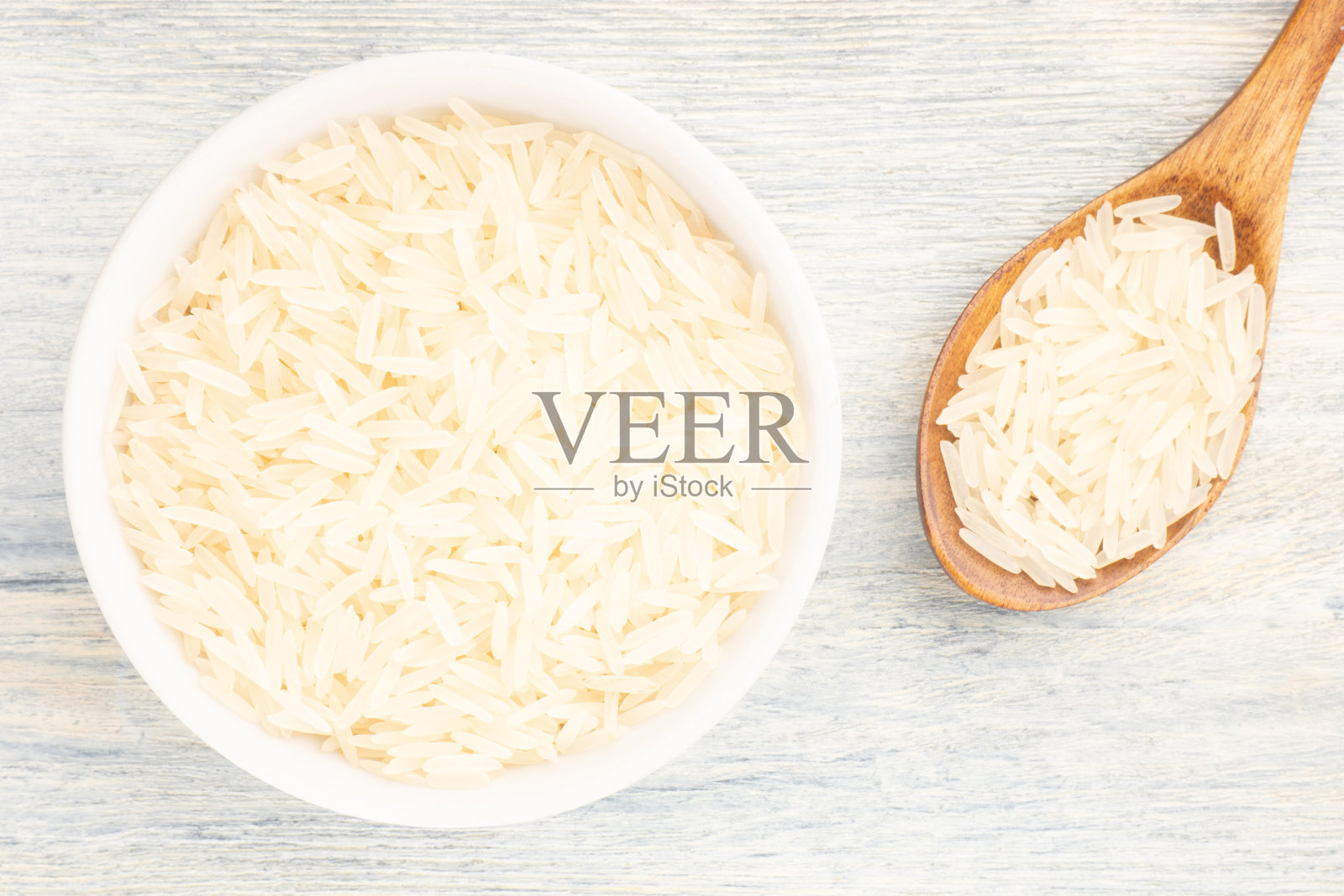 长长的印度香米放在陶瓷碗里,木勺放在白色的木制背景上。宏。平的。健康食品的概念照片摄影图片