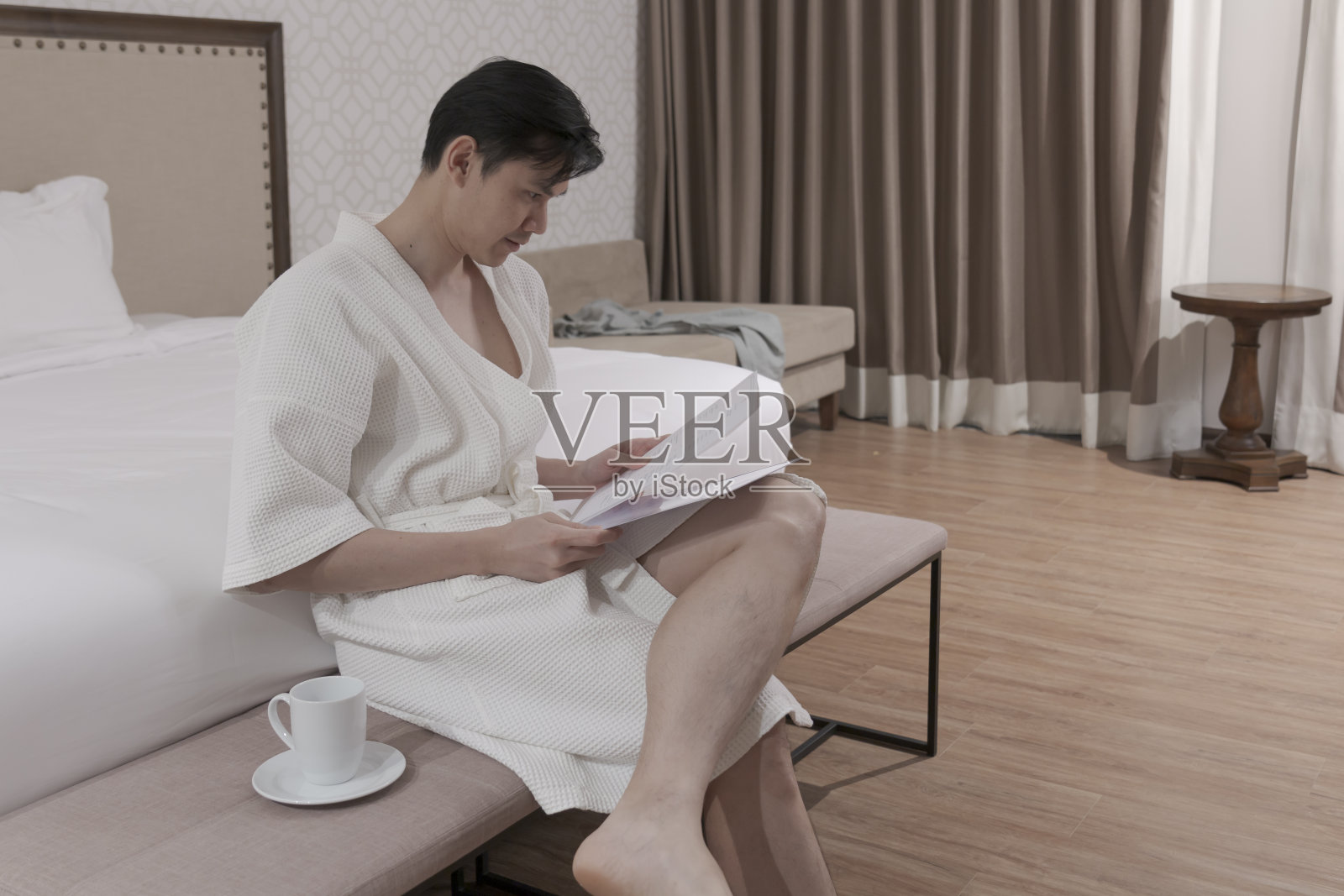 年轻男子穿着浴袍在卧室喝咖啡。男性早上喝咖啡。照片摄影图片