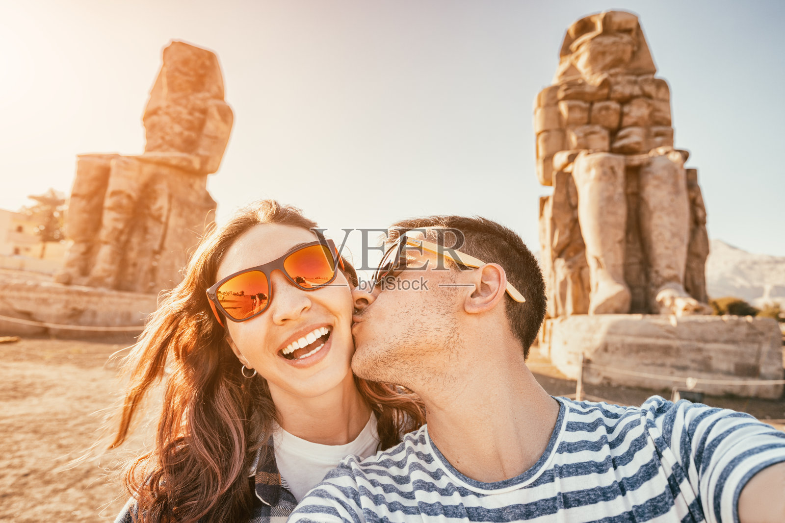 在埃及卢克索蜜月旅行期间,快乐的旅行情侣在著名的门农巨像附近自拍照片摄影图片