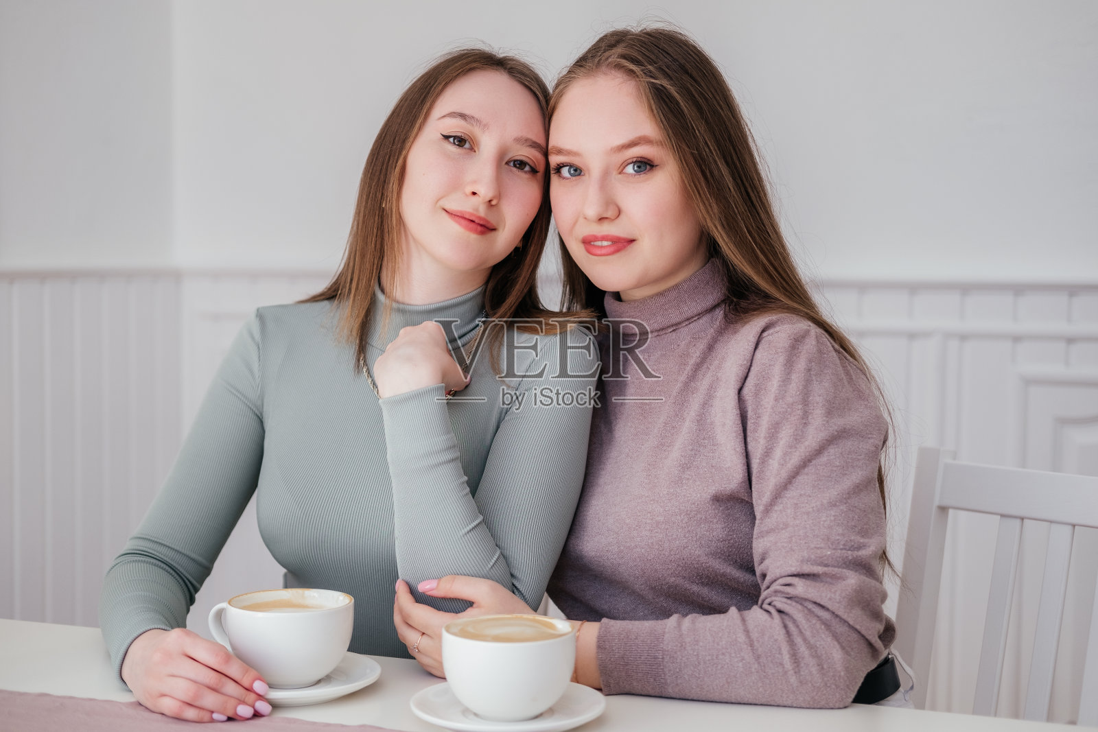 两个年轻的女性朋友坐在咖啡馆里喝着咖啡,拥抱着。微笑的白人女孩在室内聊天照片摄影图片