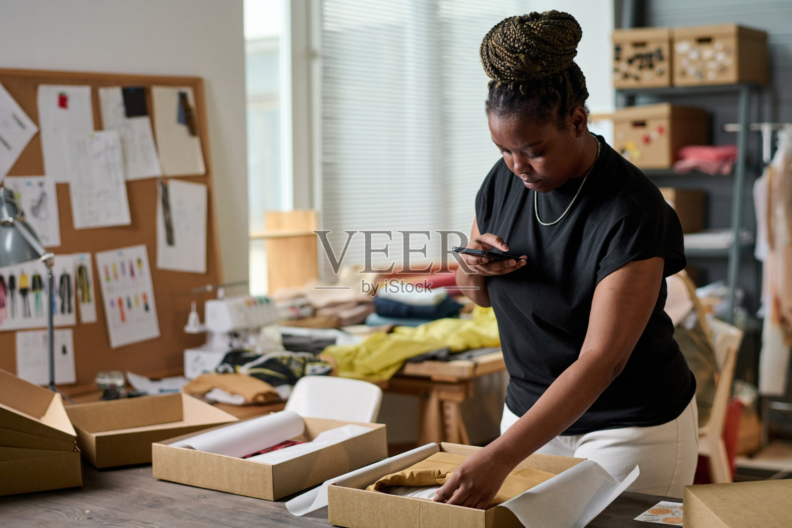 年轻的女裁缝用智能手机拍盒子里装好的衣服照片摄影图片