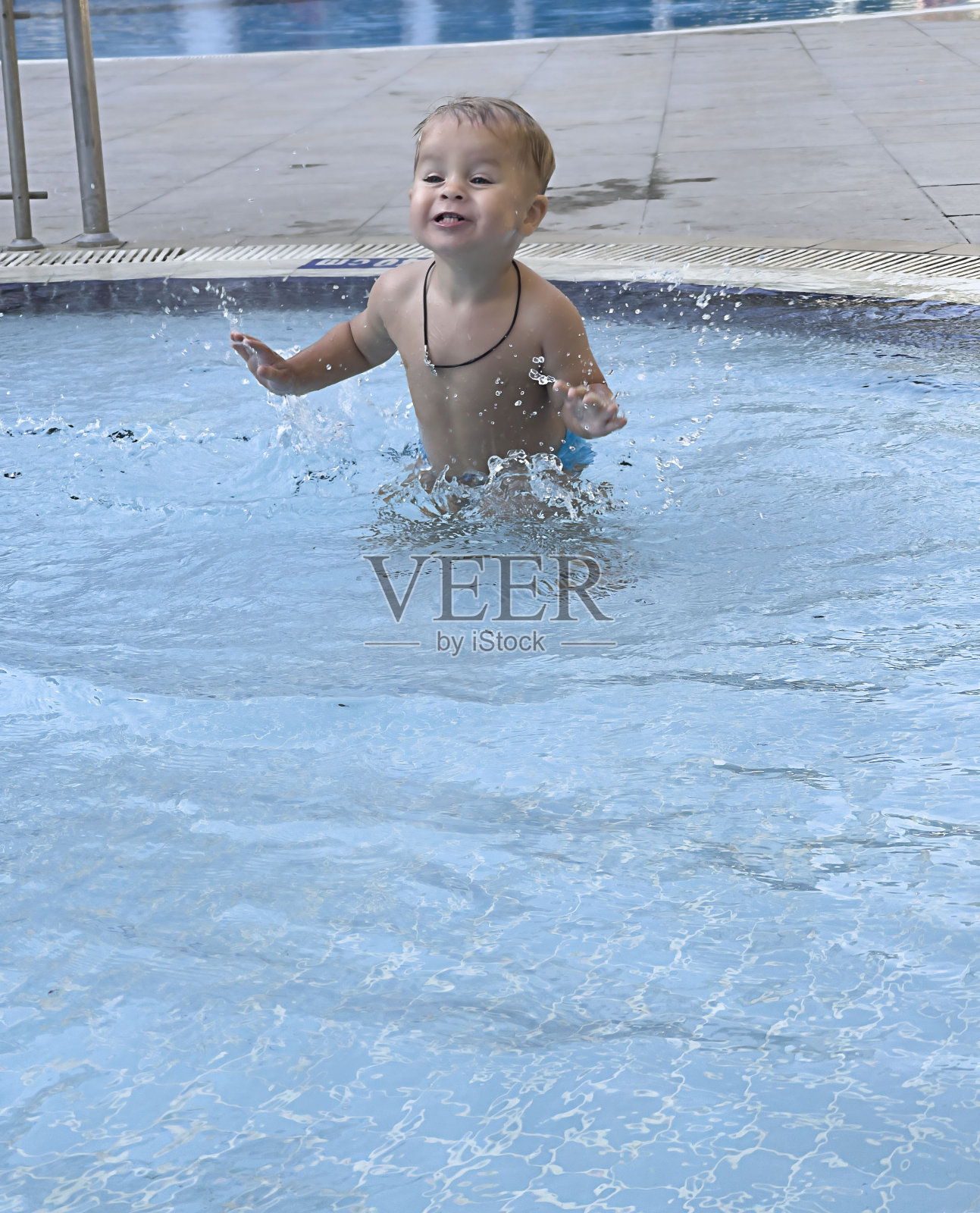 人。一个小男孩在现场的游泳池里游泳,玩得很开心,溅起了水照片摄影图片