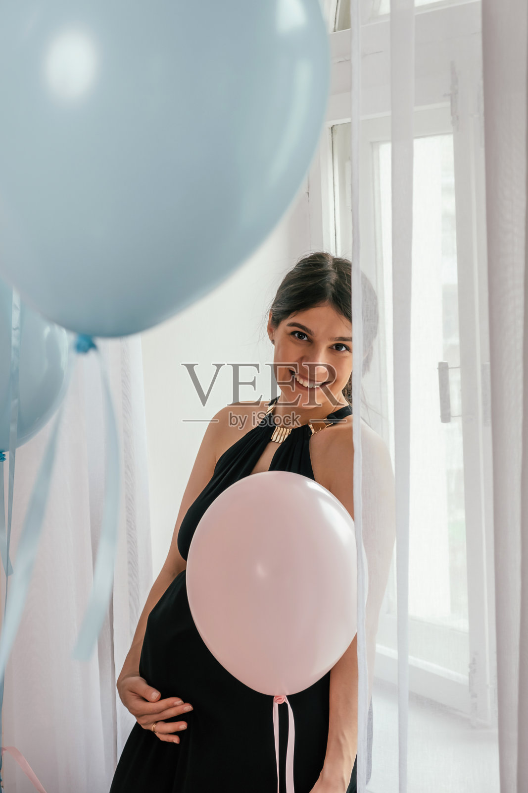 快乐美丽的黑头发年轻孕妇身穿黑色连衣裙,手里拿着一个粉红色的气球。家庭、怀孕和产前护理的概念照片摄影图片