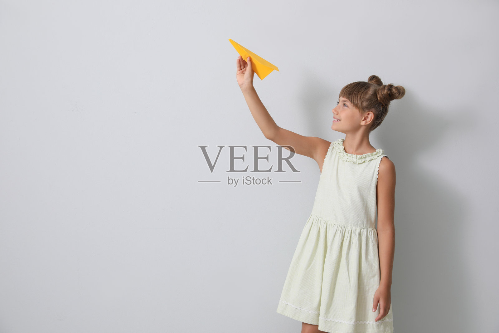 可爱的小女孩在浅灰色的背景下玩纸飞机。空间的文本照片摄影图片