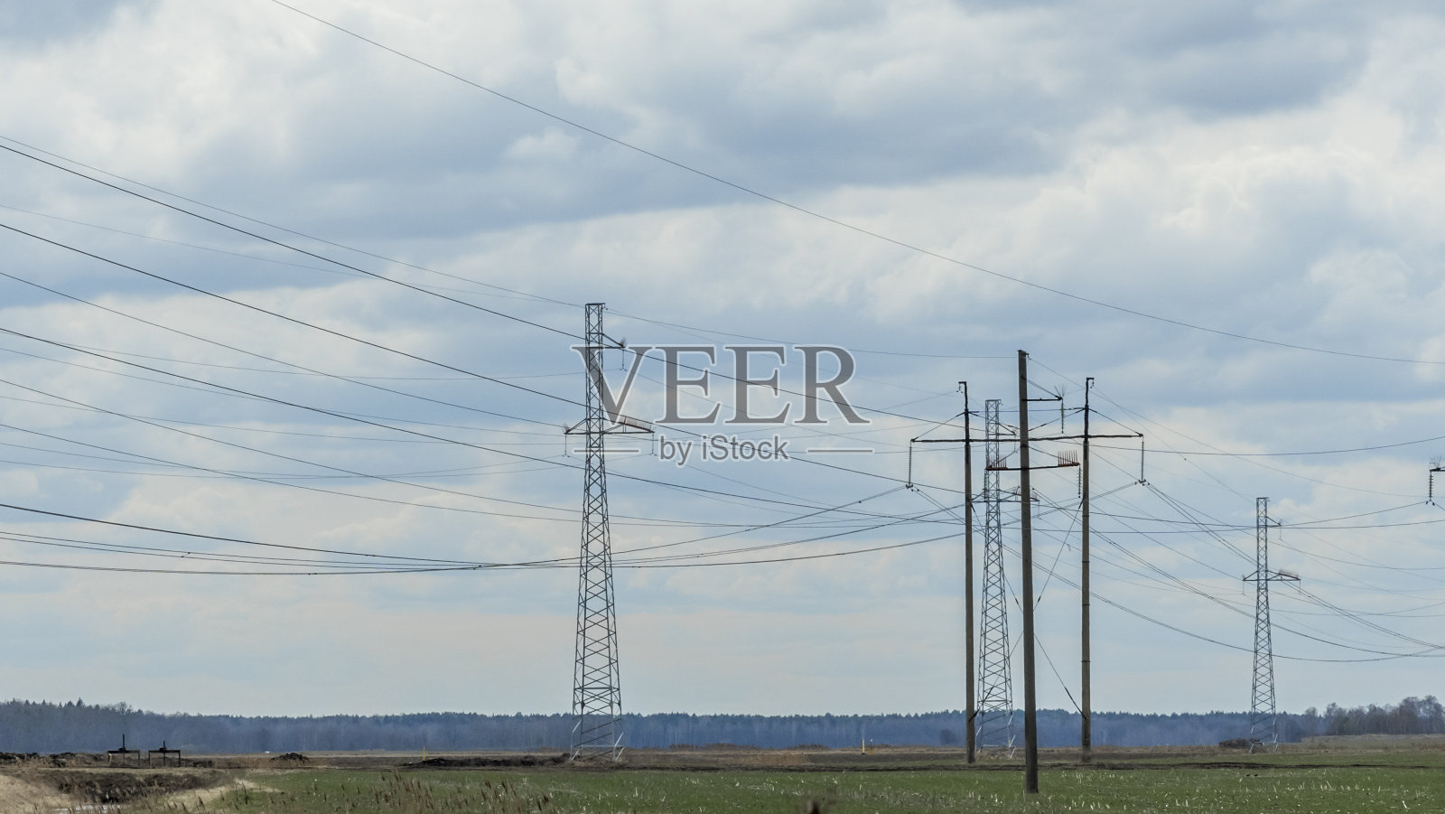 在蓝天白云背景下的高压岗位。蓝天春草上电线杆网。照片摄影图片