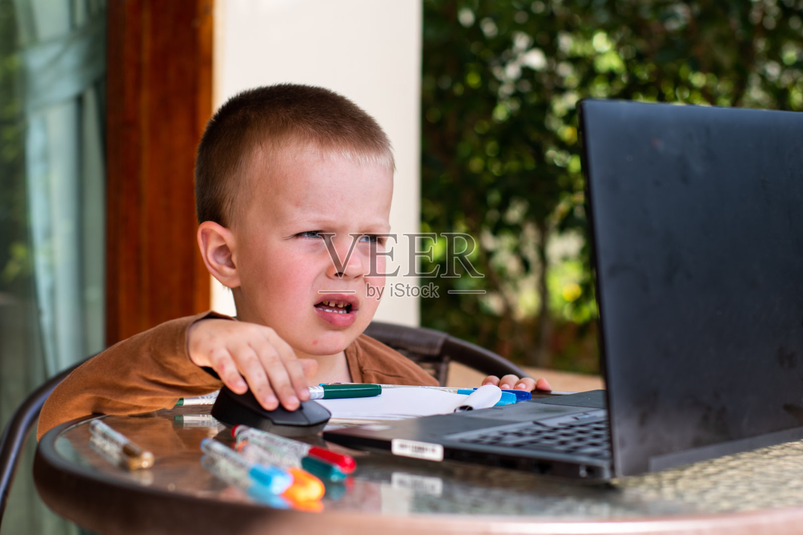 一个小孩正坐在笔记本电脑前。男孩看着监视器。照片摄影图片