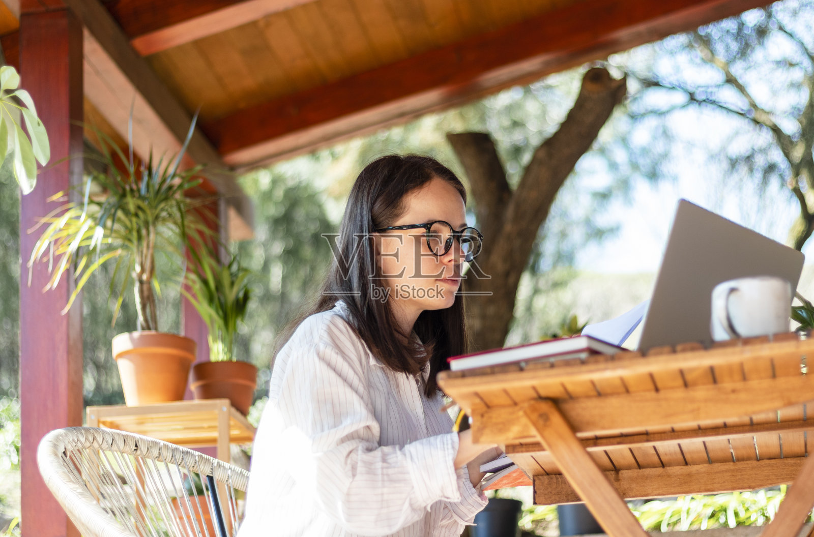 戴着眼镜、穿着白衬衫的中年妇女坐在阳台上,看着笔记本电脑。照片摄影图片