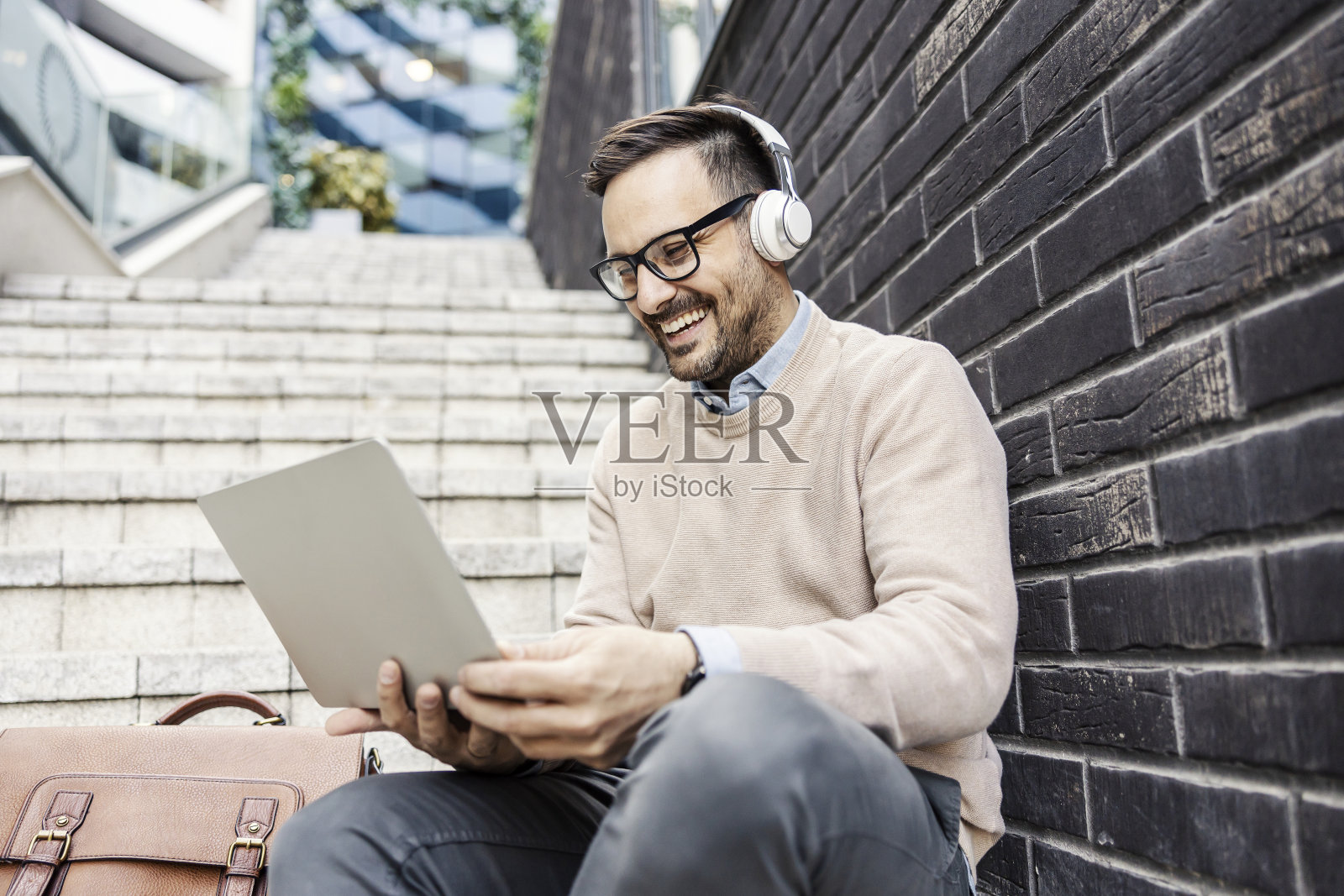 一个精明的商人坐在楼梯上,戴着耳机,用着笔记本电脑。照片摄影图片