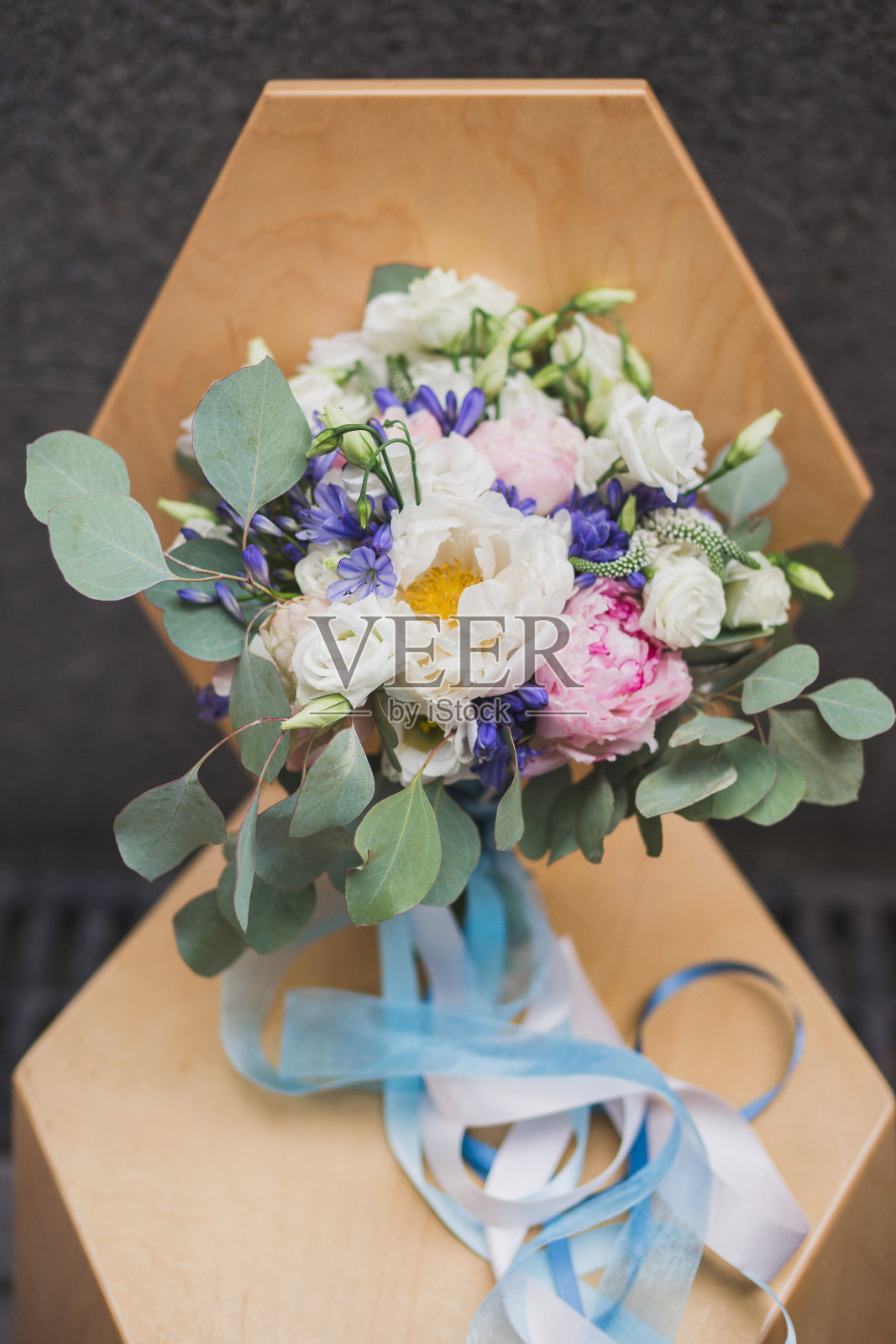 婚礼花束牡丹和桉树带着丝带站在户外灰色石墙背景下的棕色木椅上。照片摄影图片