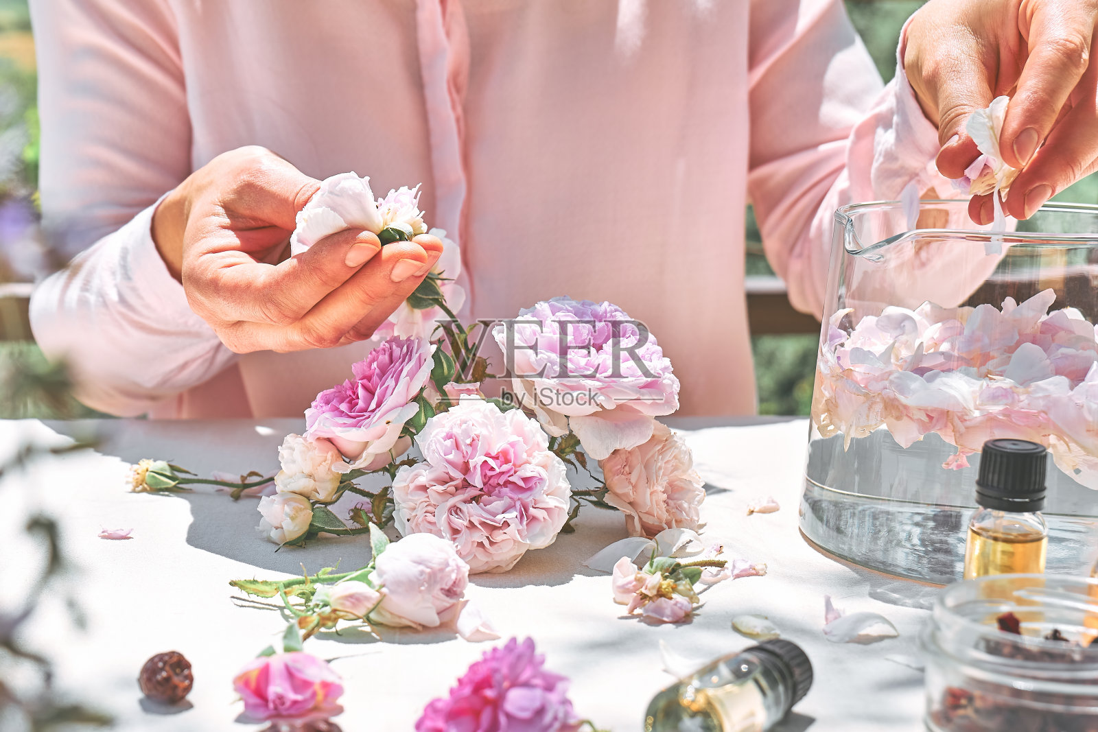 女人准备玫瑰水与粉红色的玫瑰花瓣在玻璃碗。护肤spa,天然美容治疗,自制化妆品。有选择性的重点。照片摄影图片