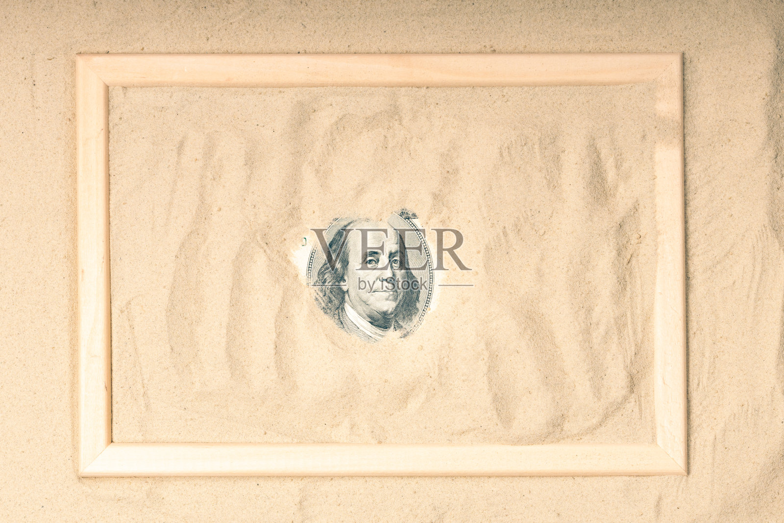 100美元钞票上的总统从沙子里探出头来的肖像。在美元周围的沙滩上有一个木制的框架照片摄影图片