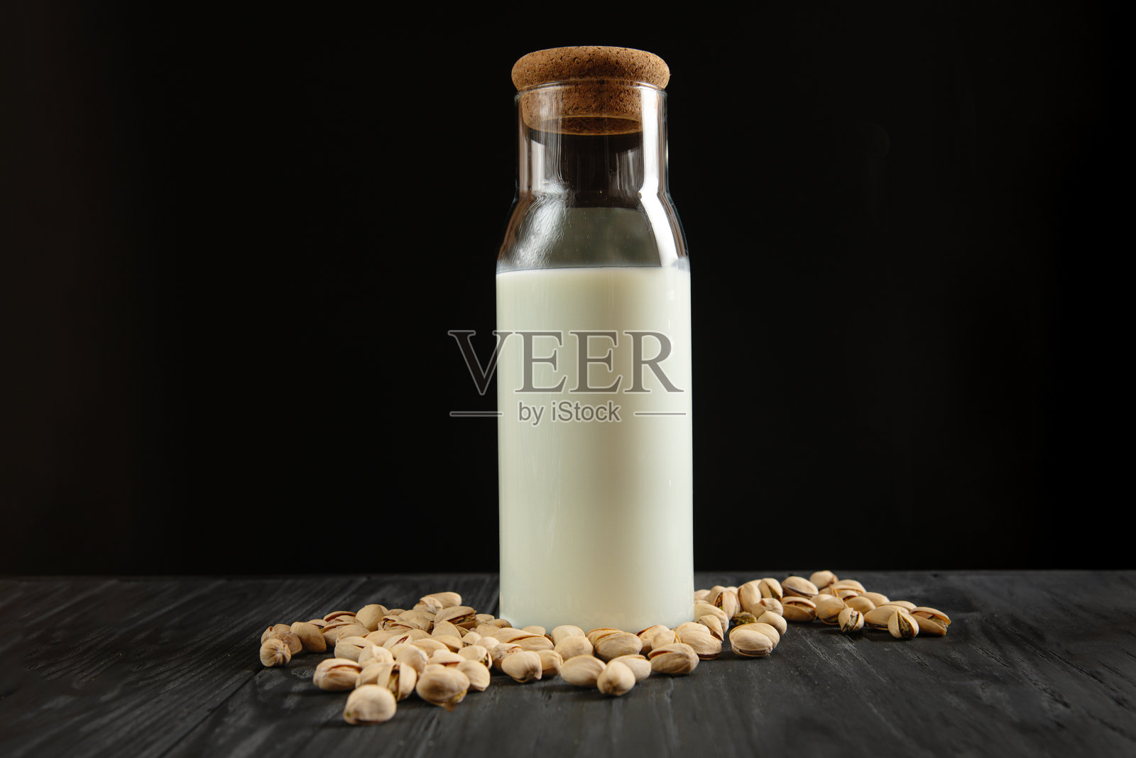 黑色背景上放着一瓶开心果牛奶照片摄影图片