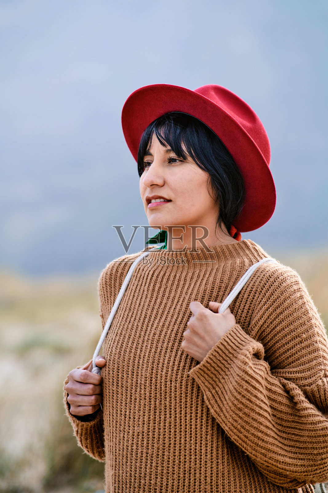 肖像的拉丁裔妇女在红色帽子拿着她的背包在自然照片摄影图片