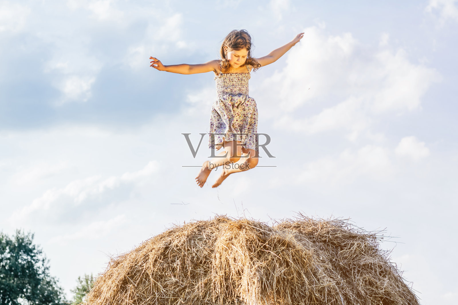 小女孩在田野里的草堆上玩耍和跳跃的肖像。高反弹。到达天空。低角度。一个孩子在操场上照片摄影图片