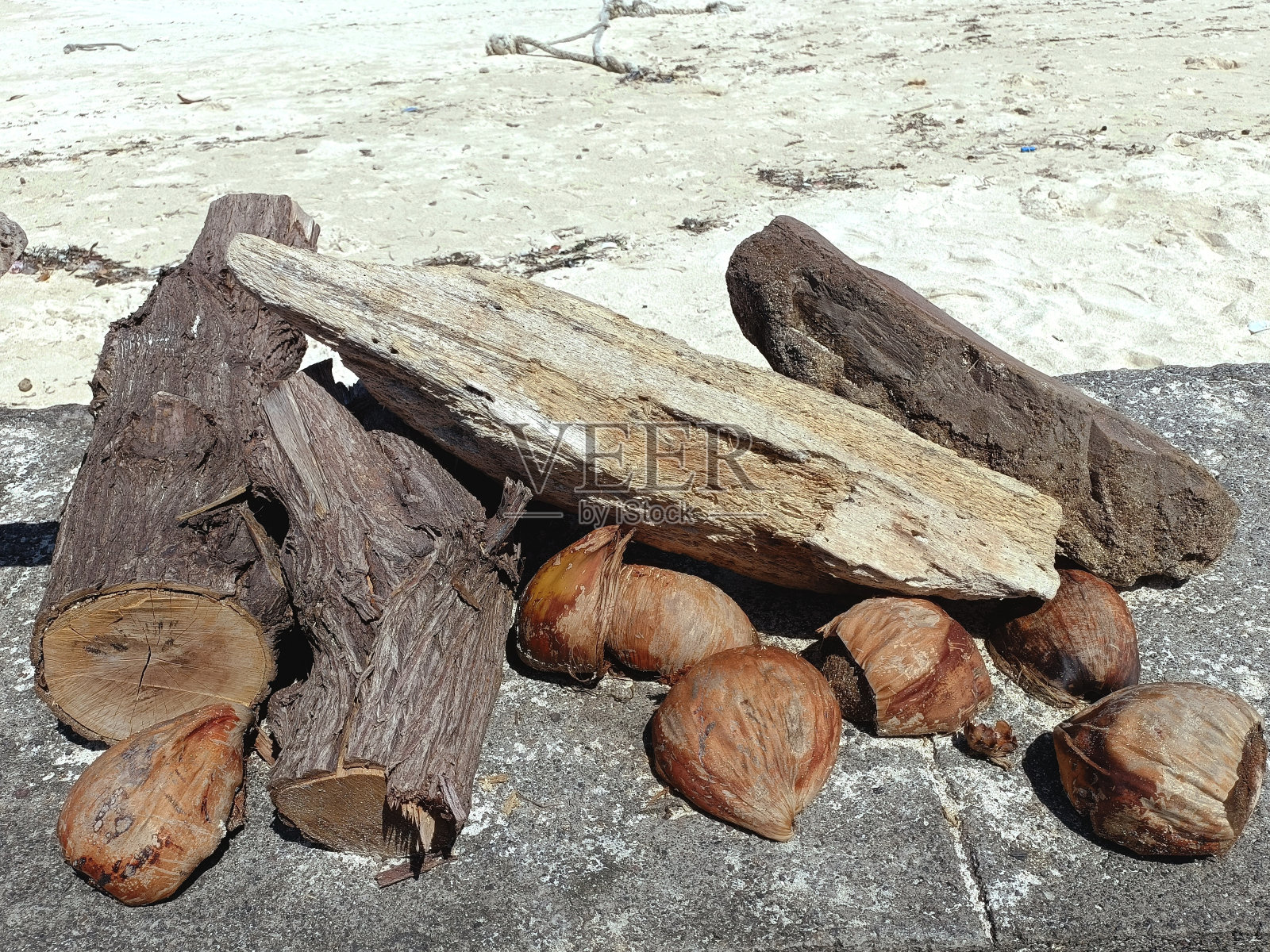 木柴、浮木和椰子壳堆在石墙上,背景是沙滩照片摄影图片