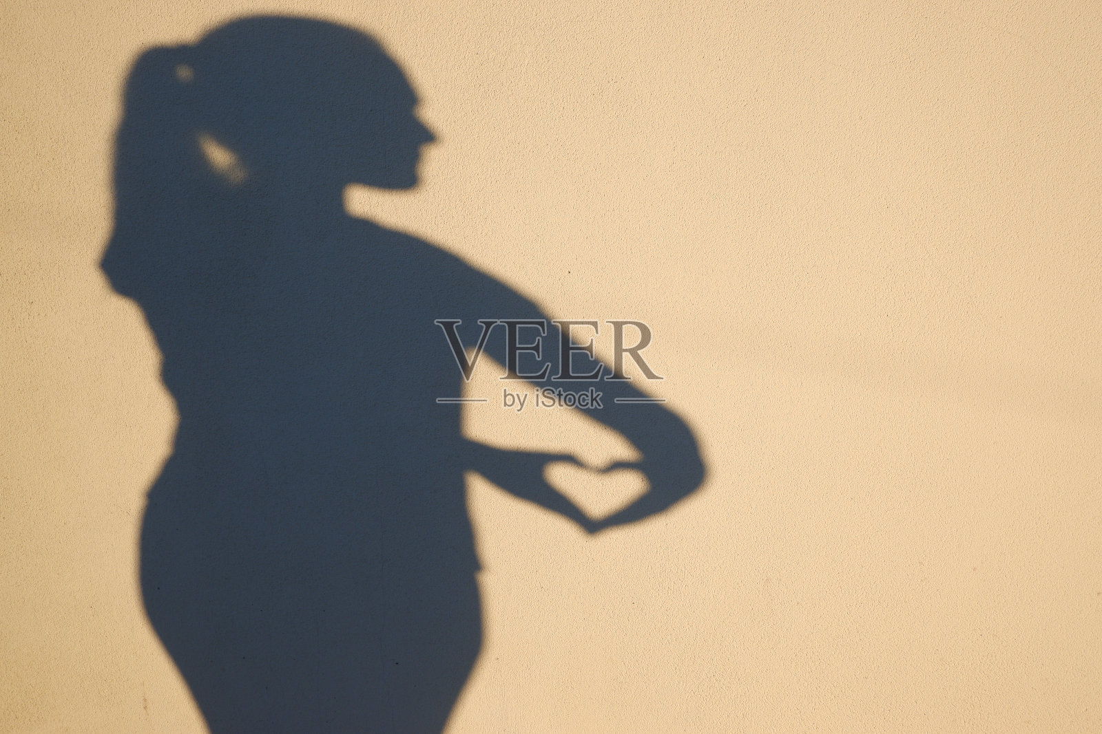 照片的影子的一个女性的形象。那个女人把双手交叉成心形。浪漫和爱情。照片摄影图片