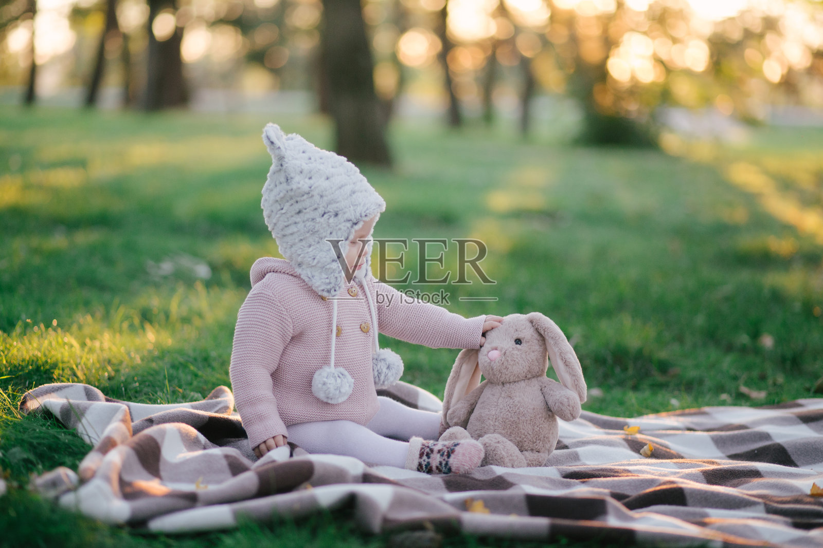 可爱时髦的小宝贝拿着玩具坐在草地上。照片摄影图片