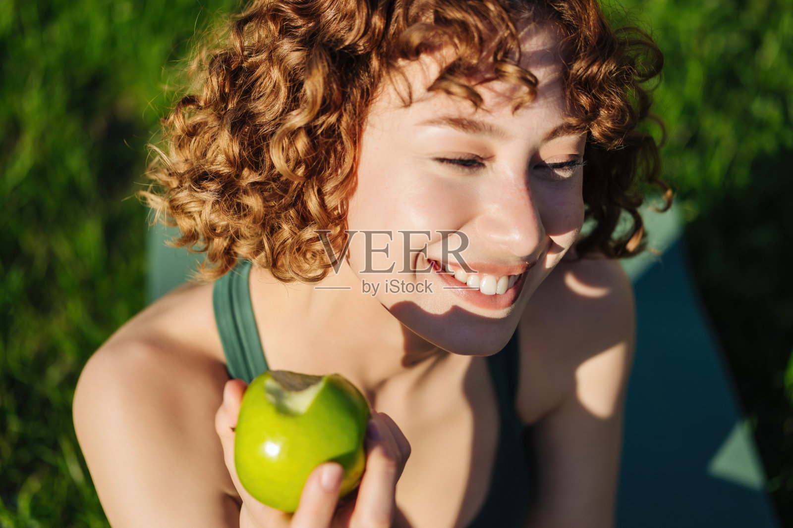 健康、运动、运动的年轻女子微笑着吃青苹果。女人在休息时吃苹果。为健身女孩准备的健康零食。照片摄影图片