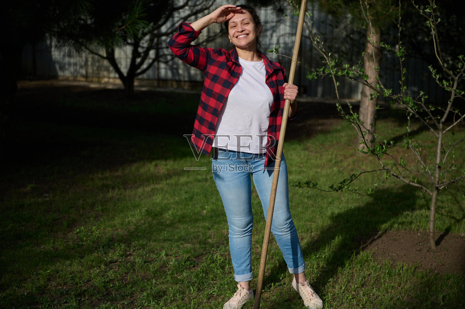 笑容满面的女园丁站在后院,手里拿着一件园艺工具照片摄影图片
