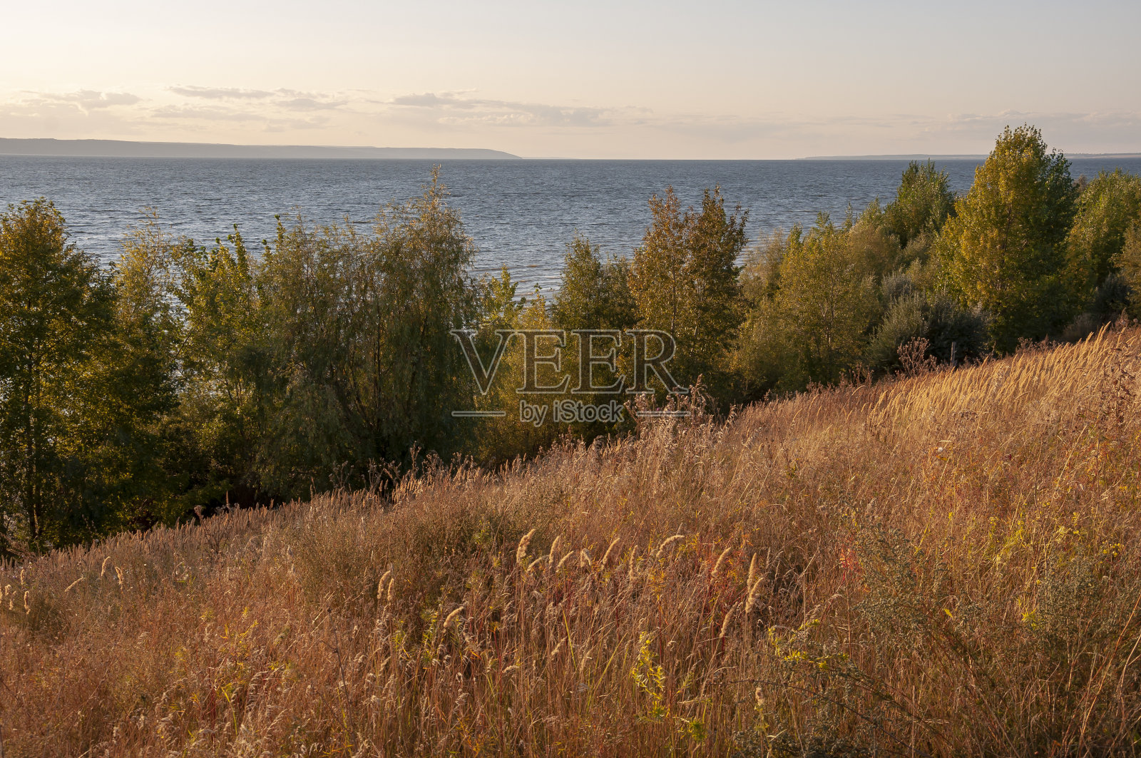 从高地看湖的景色。树木和灌木生长在它的周围。落日的余晖从树叶中透出照片摄影图片