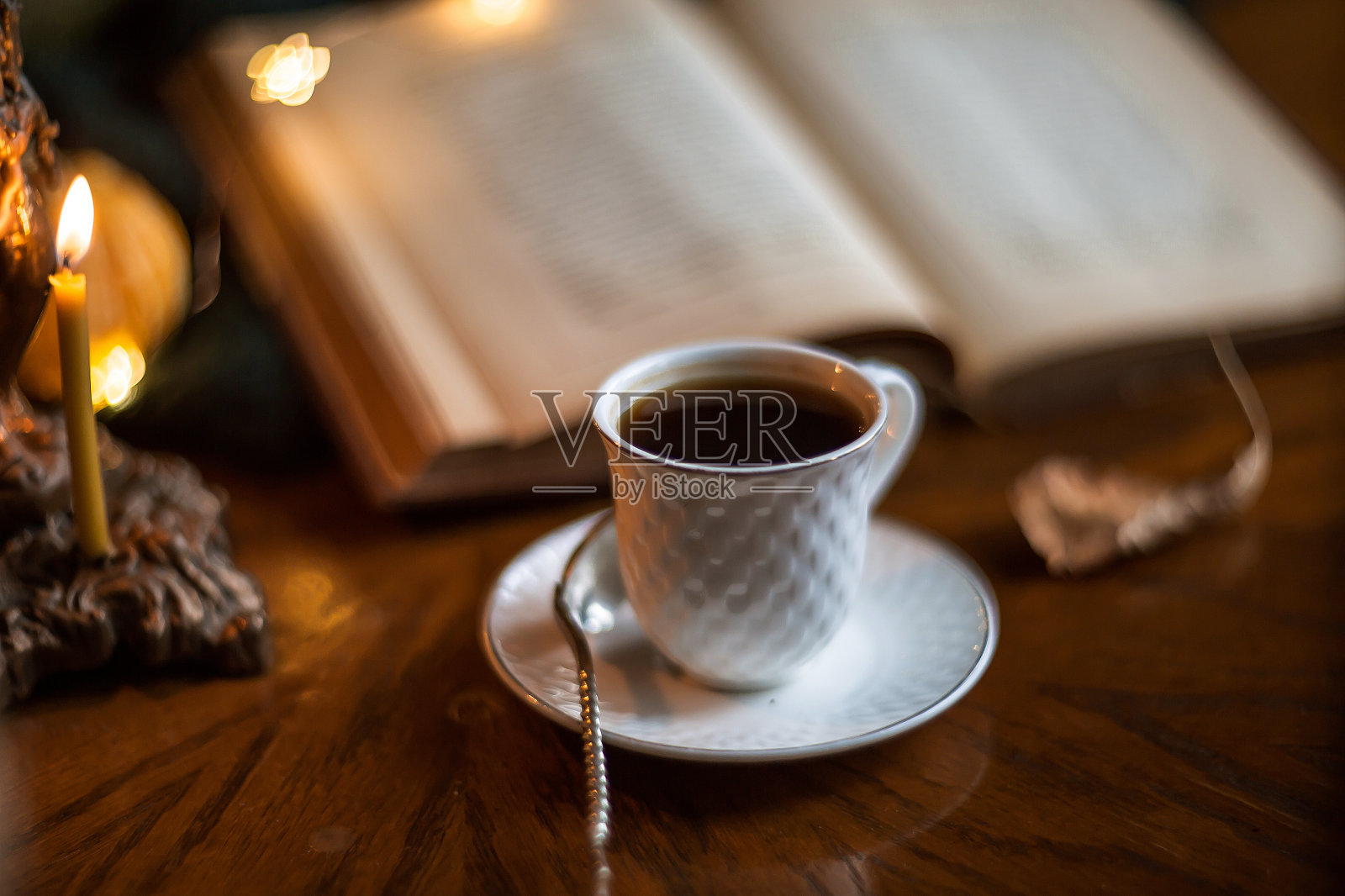 秋天静物与美丽的散景。一杯咖啡和一本书透过潮湿的玻璃放在木桌上。照片摄影图片