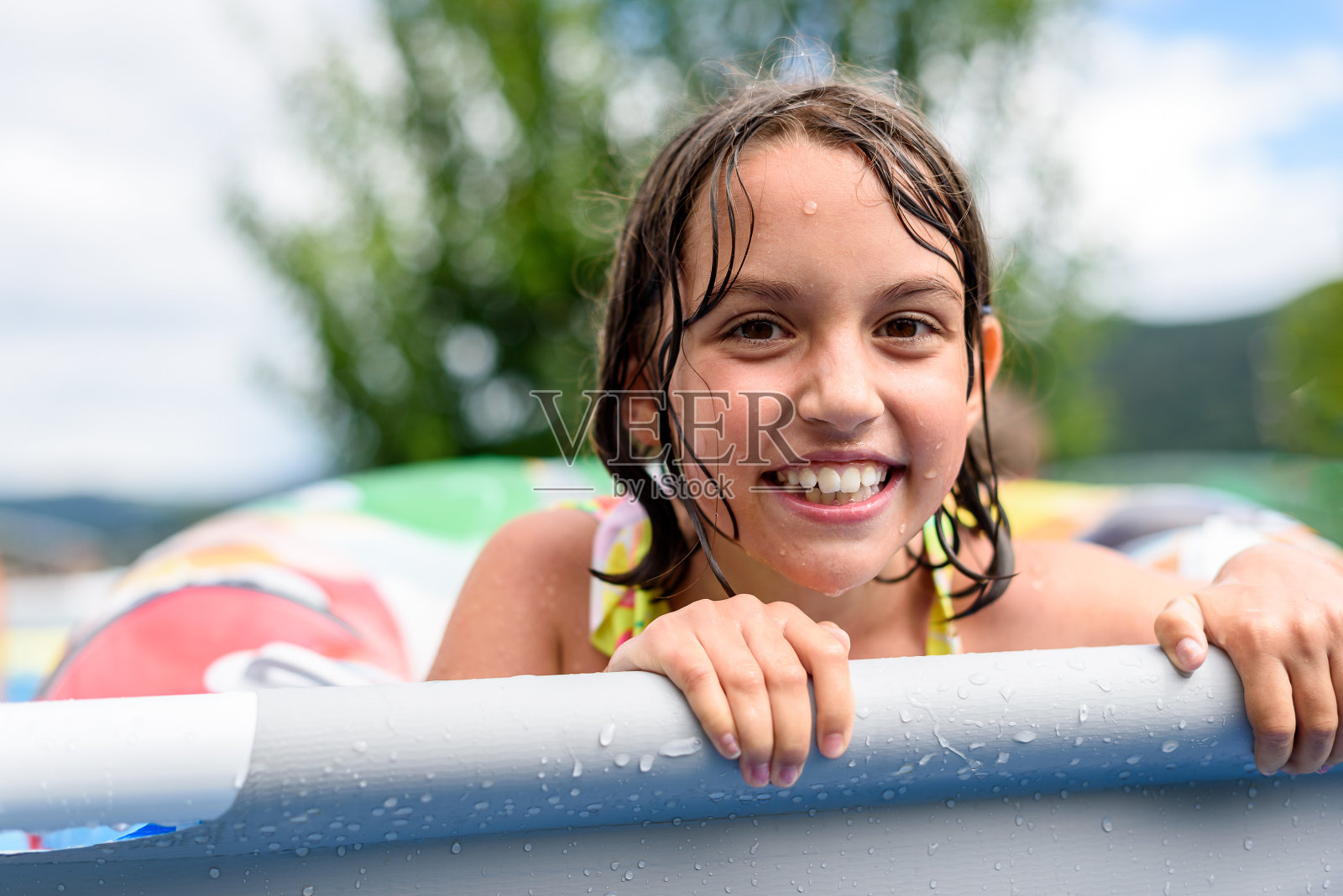 夏天,孩子们在家里的游泳池里玩耍。女孩们正在后院或前院的游泳池里享受暑假。孩子们在洒水,笑着,玩得很开心。照片摄影图片