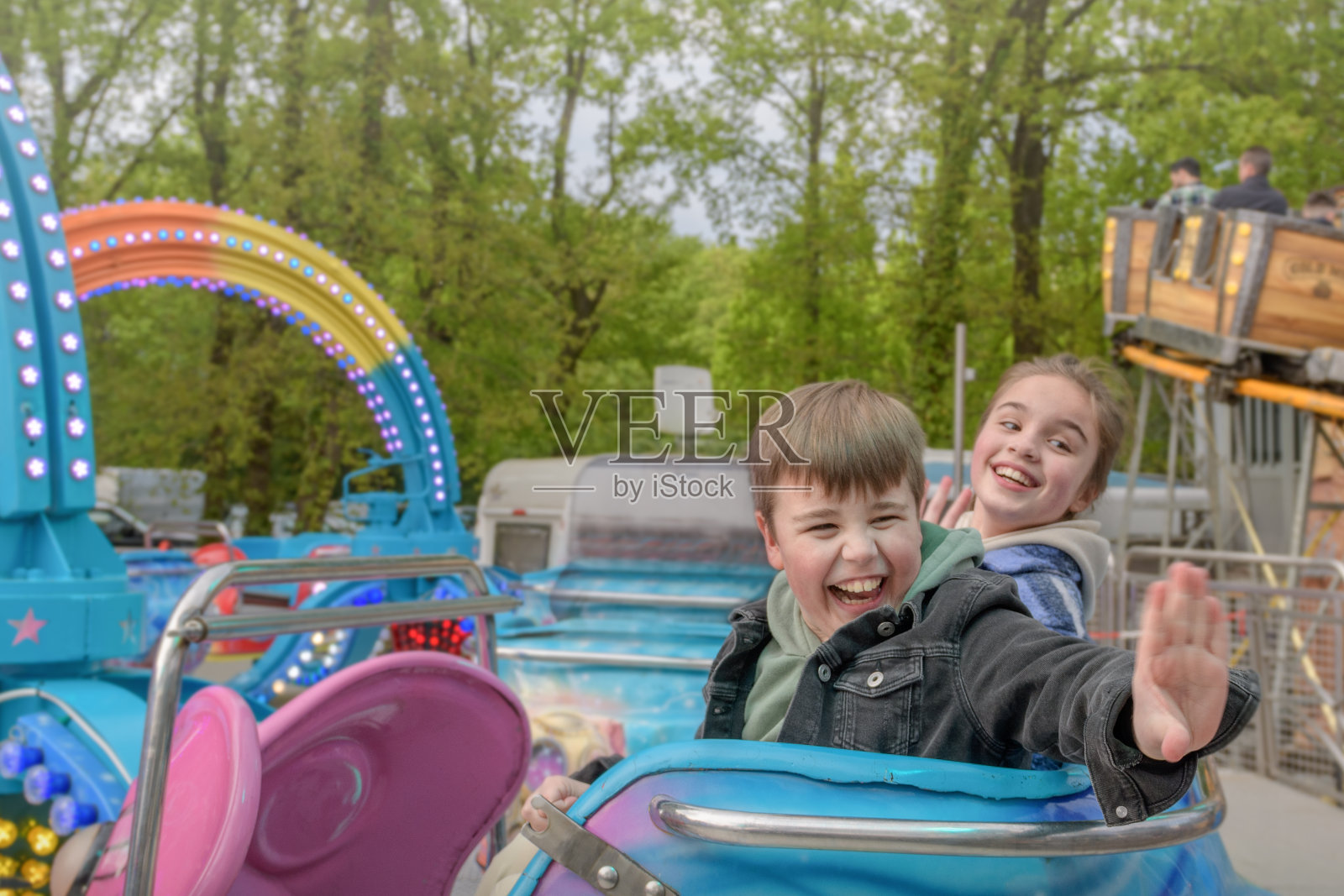 在游乐园的旋转木马上,一个女孩和一个男孩带着真正积极的情绪。照片摄影图片