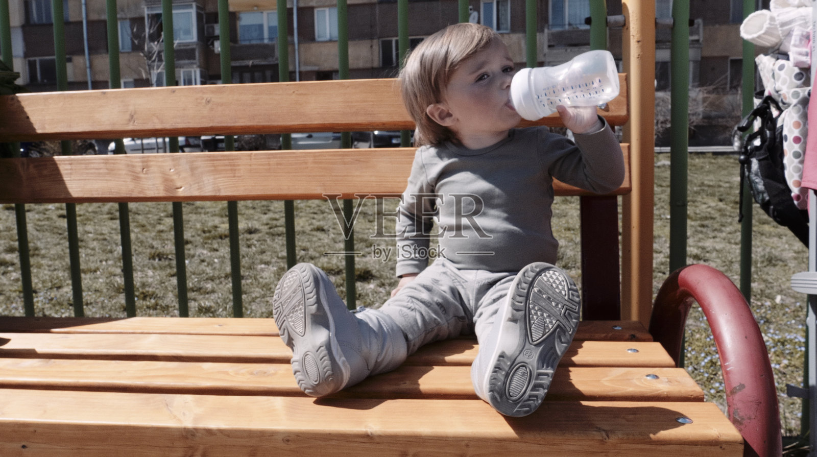 春天,婴儿在操场上玩耍时喝水。照片摄影图片