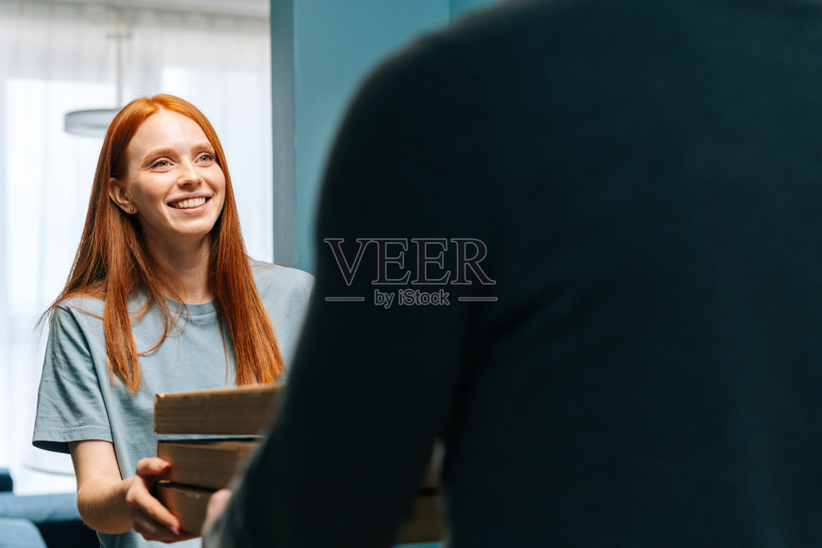 微笑的年轻女子收到纸盒与热披萨从不知名的送货员在家门口家门口。照片摄影图片