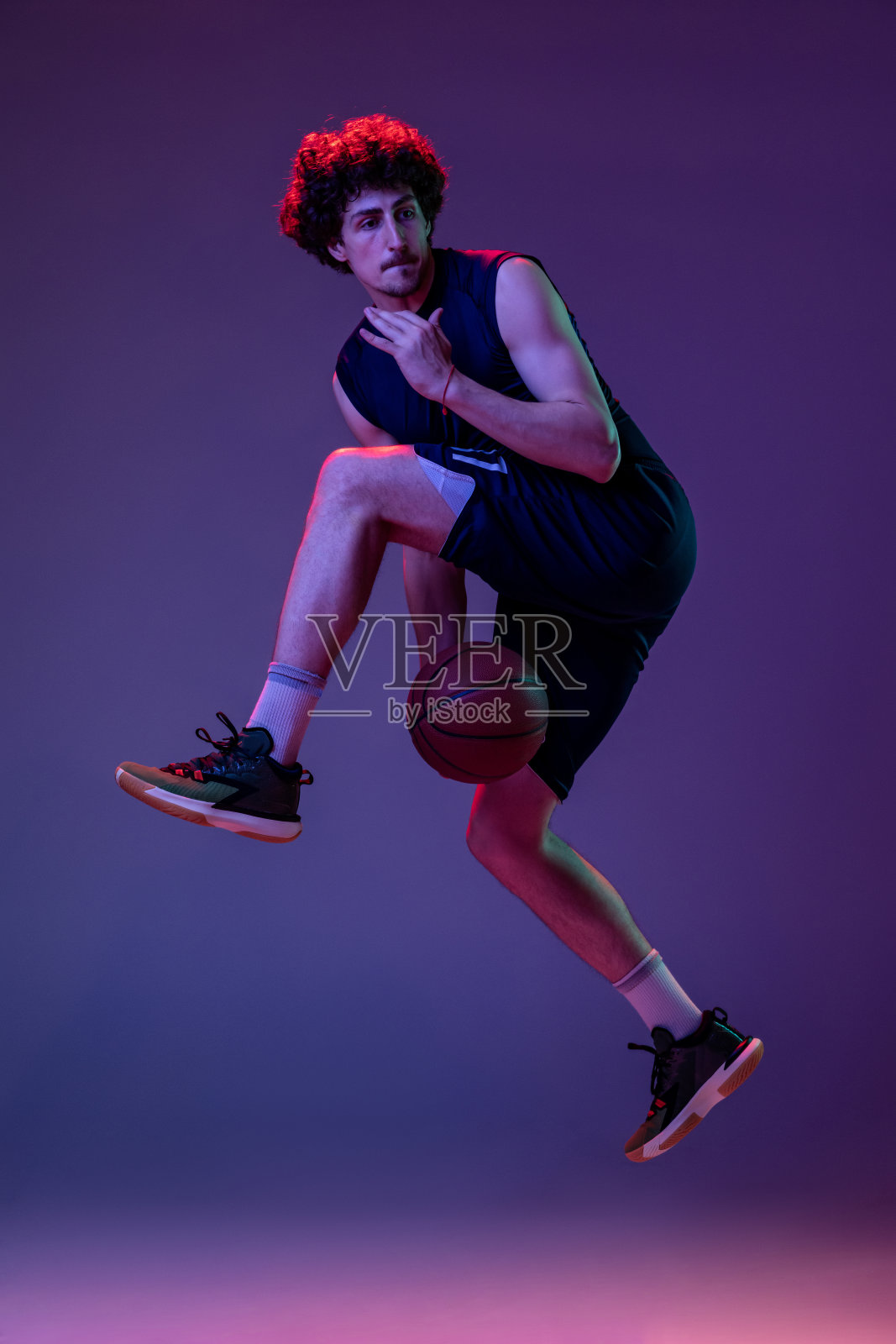 动态肖像的职业篮球运动员跳跃与球孤立的紫色背景在霓虹灯。体育、艺术、创作、竞赛的概念。照片摄影图片