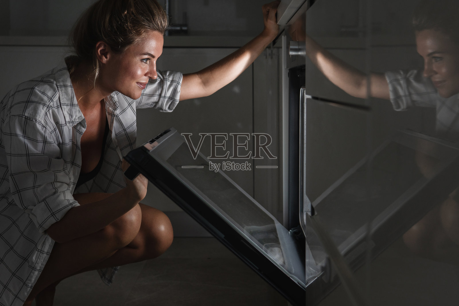 年轻漂亮的女人在检查烤箱里的糕点照片摄影图片