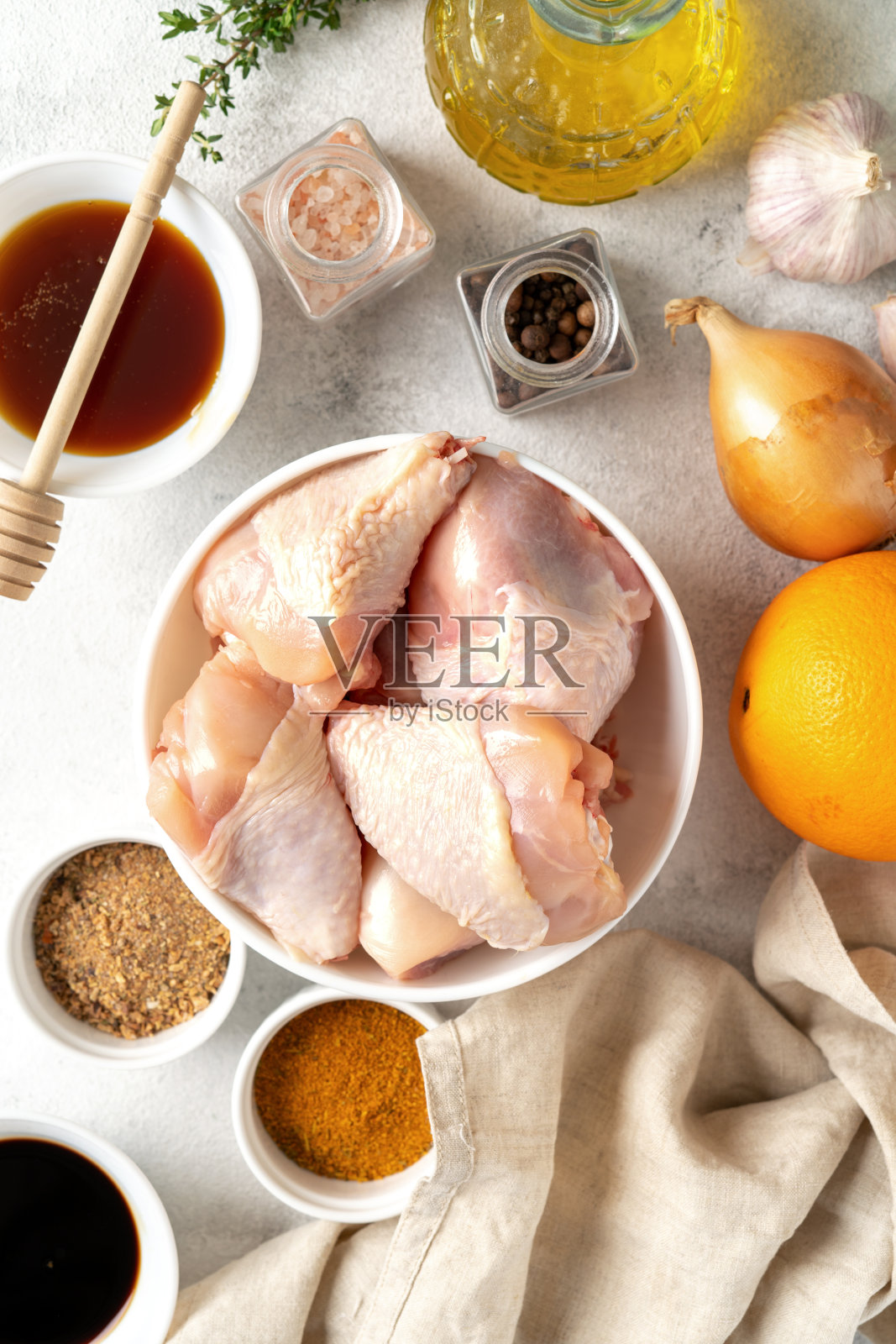 生鸡腿和香料在浅灰色的烹饪背景。准备腌制生禽肉和调味料。俯视图照片摄影图片