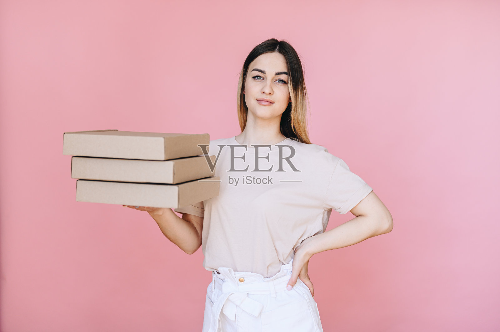 一个女孩的肖像拿着披萨盒在她的手,看着相机,手放在她的臀部照片摄影图片