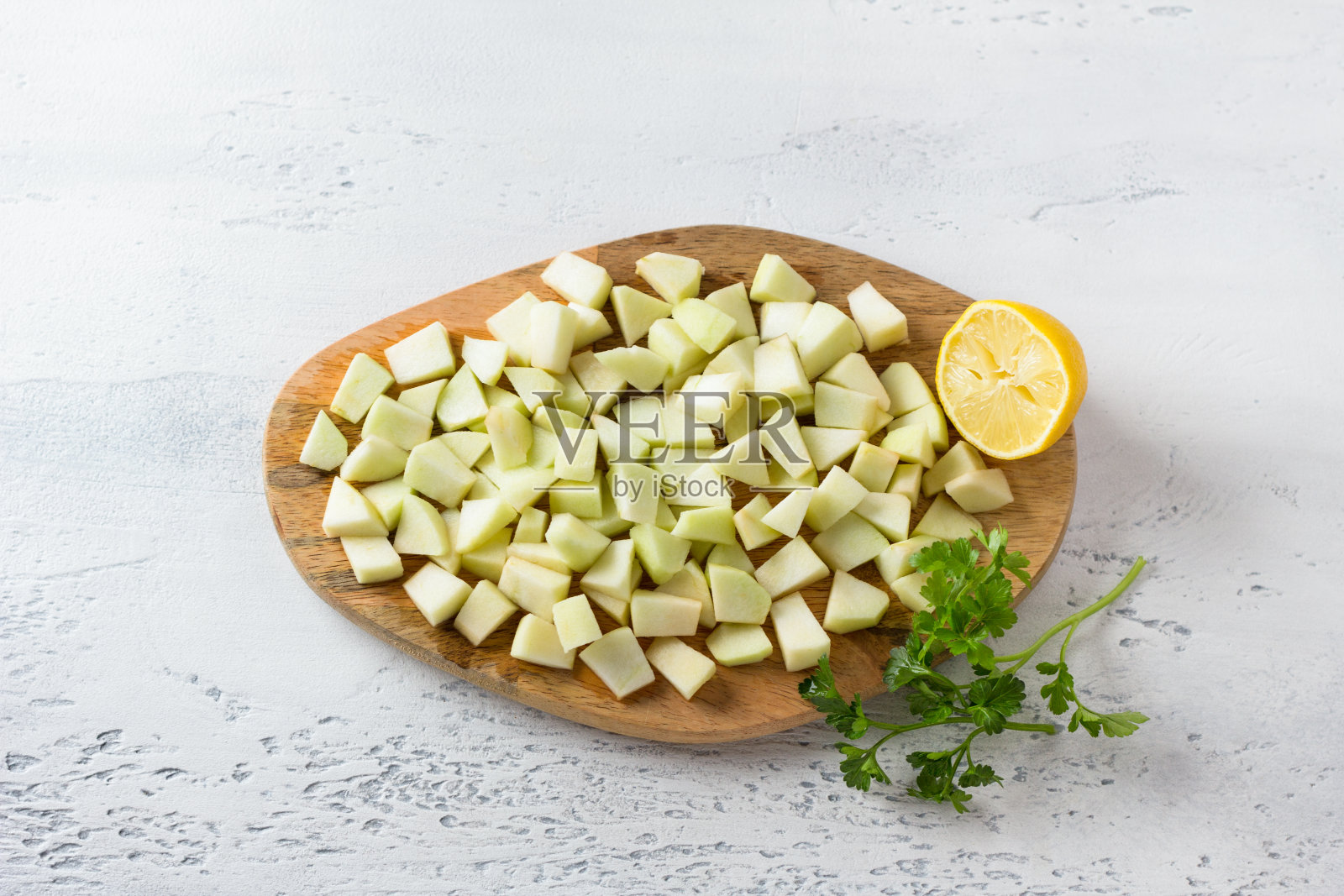 木板上有切好的苹果片做沙拉,洒上柠檬汁,半个柠檬和欧芹小枝在浅蓝色的背景上,俯视图。制作美味的素食沙拉照片摄影图片