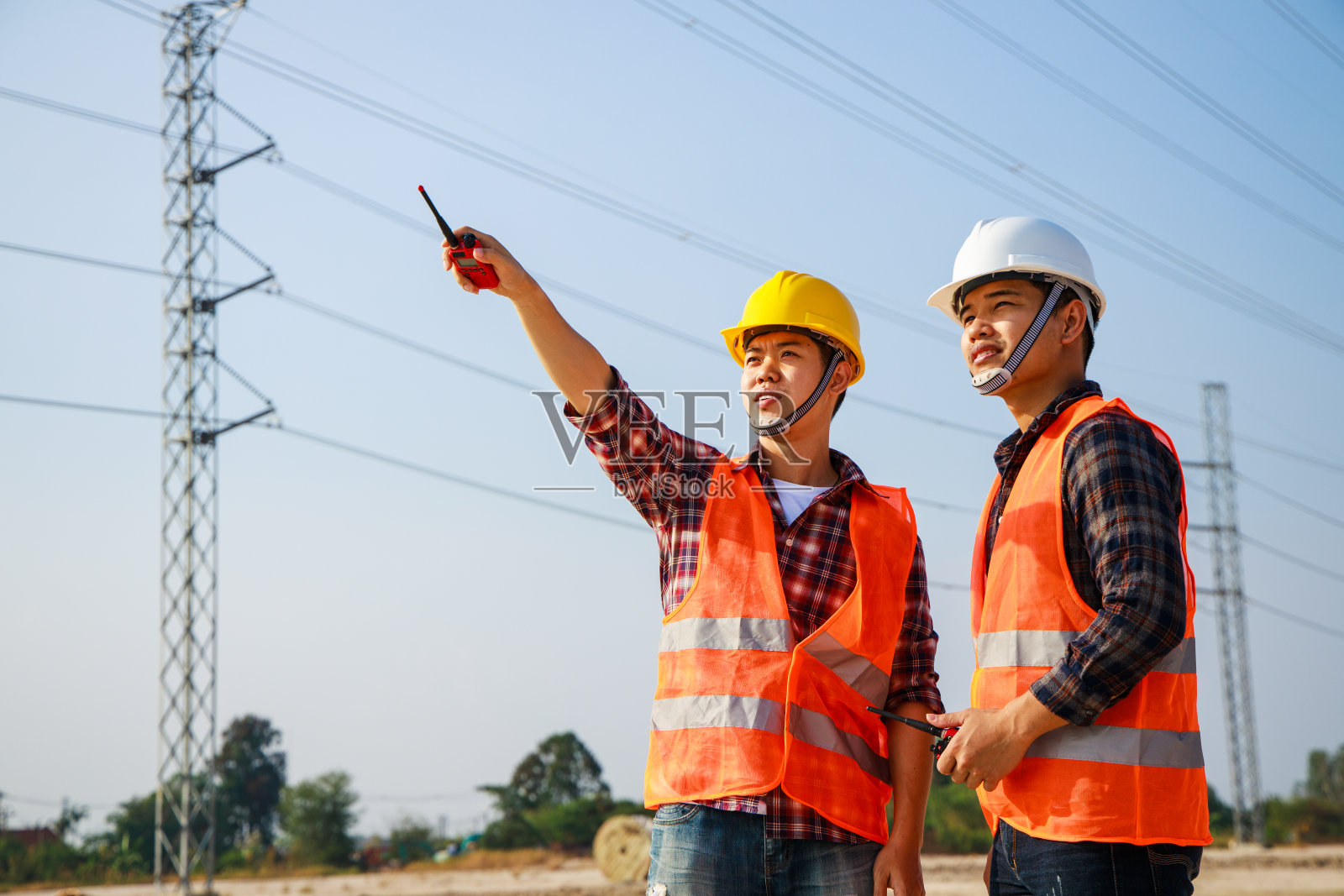 两个电气工程师与一个高压电力塔在日落的背景。照片摄影图片