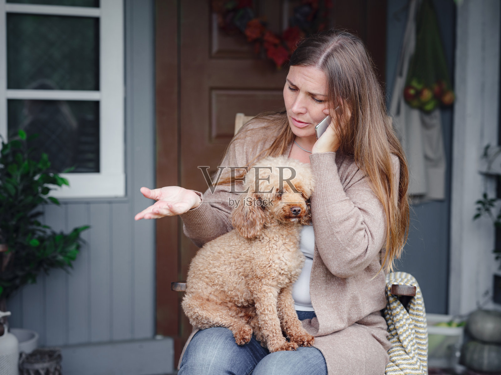女人坐在阳台上与贵宾犬交流智能手机。照片摄影图片