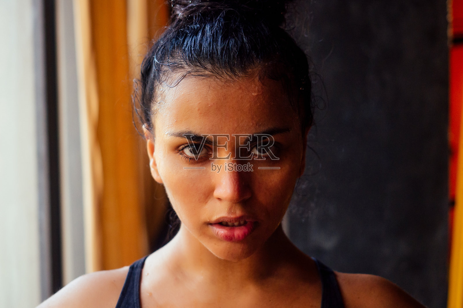 拉丁美洲的健身模特穿着胸衣和打底裤,看起来很累,额头上有汗水,在黑暗的健身房照片摄影图片