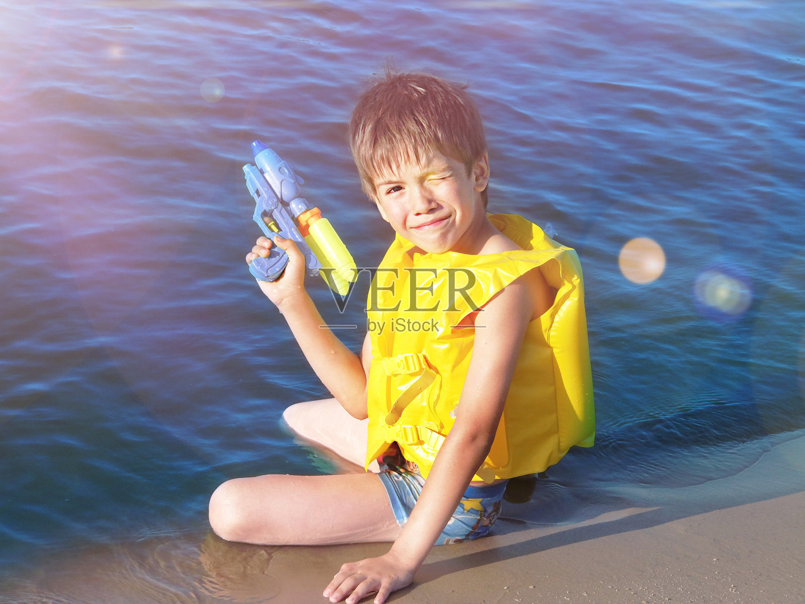 一个穿着救生衣拿着水枪的男孩在海边照片摄影图片